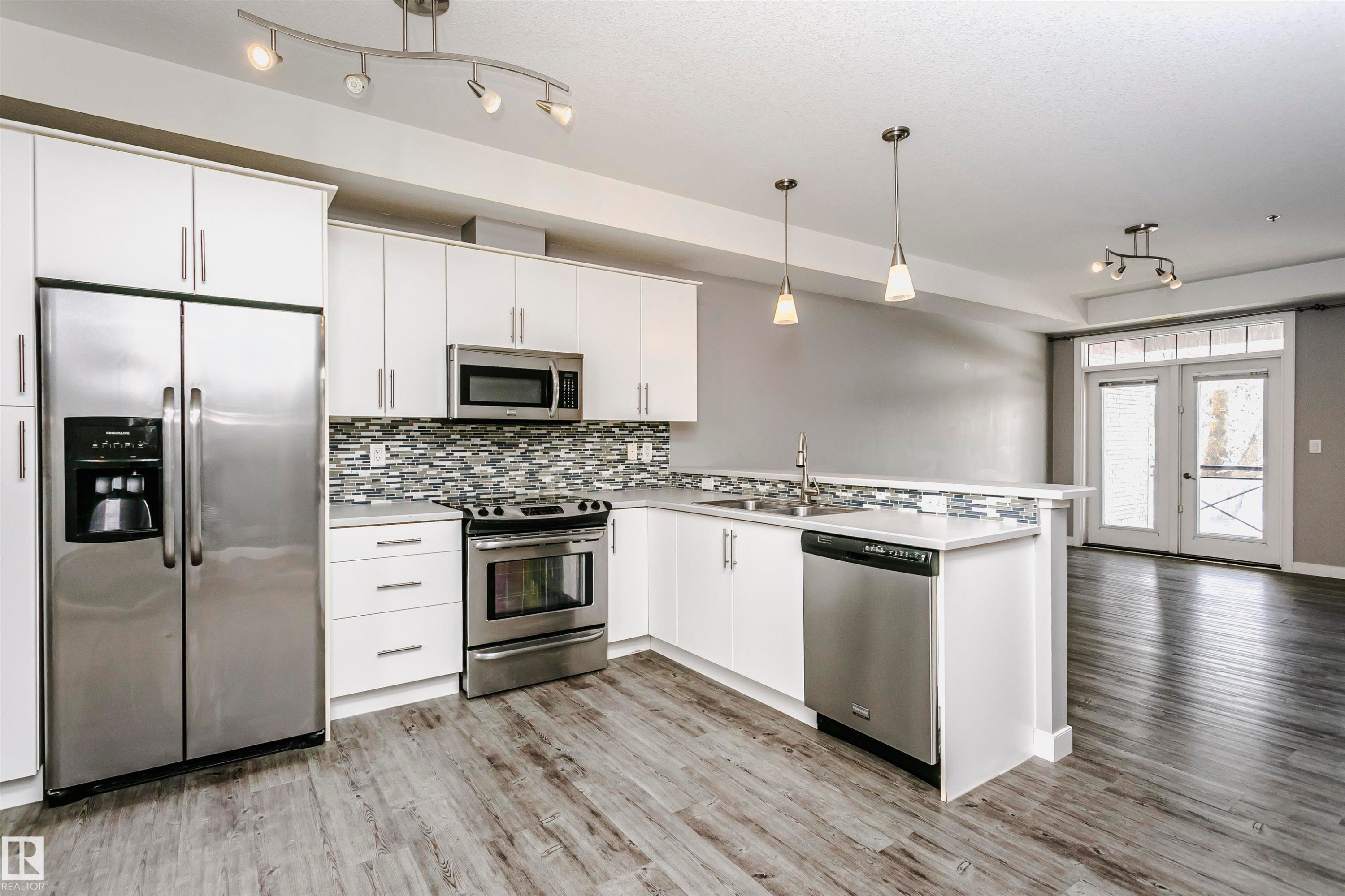 Modern kitchen featuring white cabinetry, stainless steel appliances, a tile backsplash, light countertops, and wood-finish flooring - 211 10808 71 Avenue, Edmonton, AB