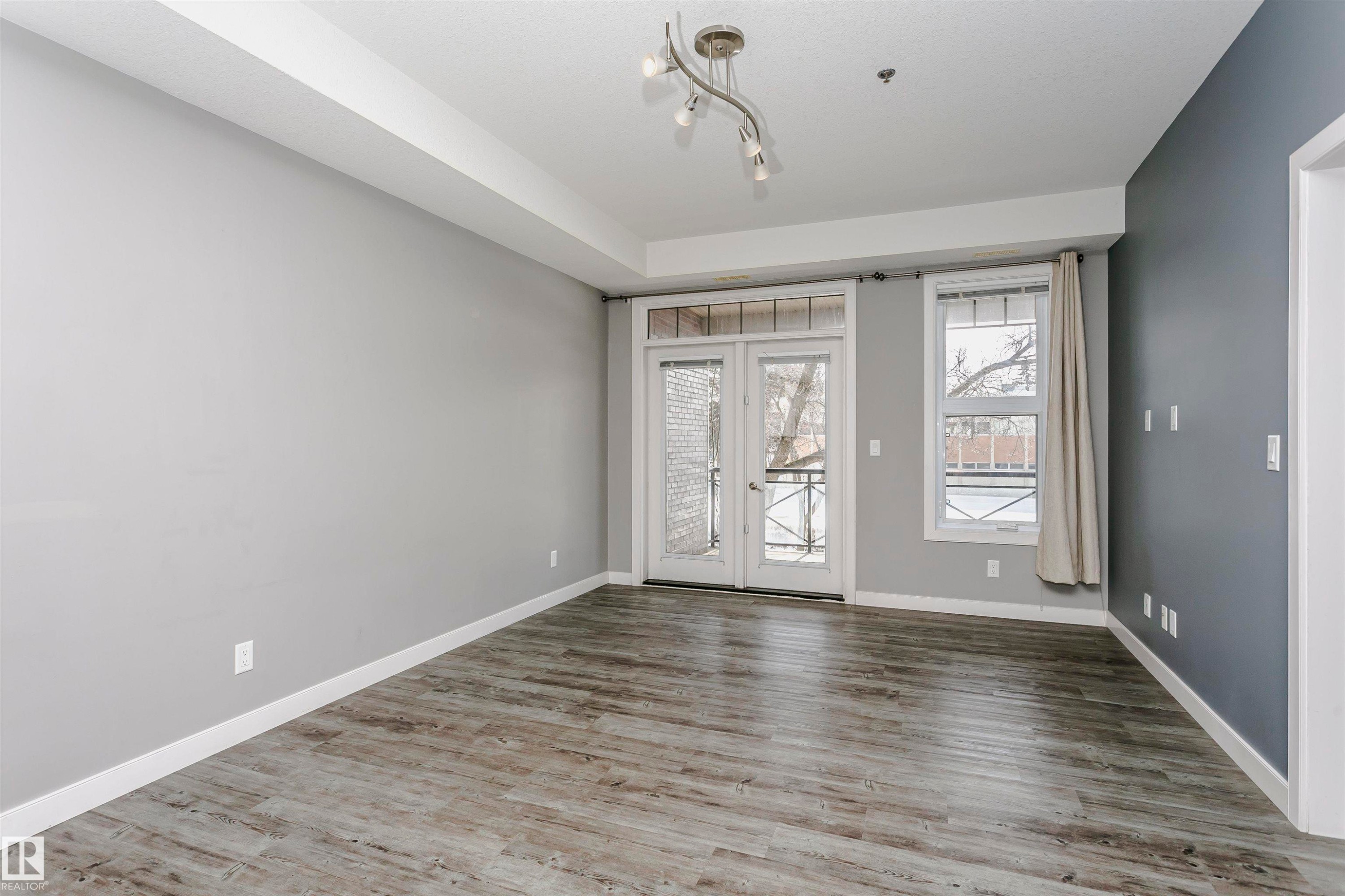 Bright living space featuring wood-finish flooring, a contemporary track light fixture, and a two-tone paint scheme - 211 10808 71 Avenue, Edmonton, AB
