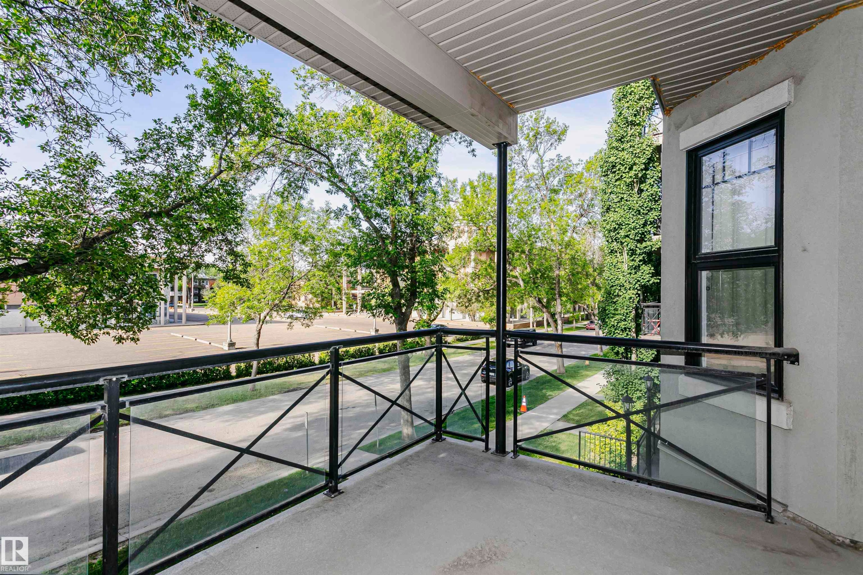 Private balcony featuring a concrete floor, black metal railing with glass inserts, and an overhead soffit - 211 10808 71 Avenue, Edmonton, AB