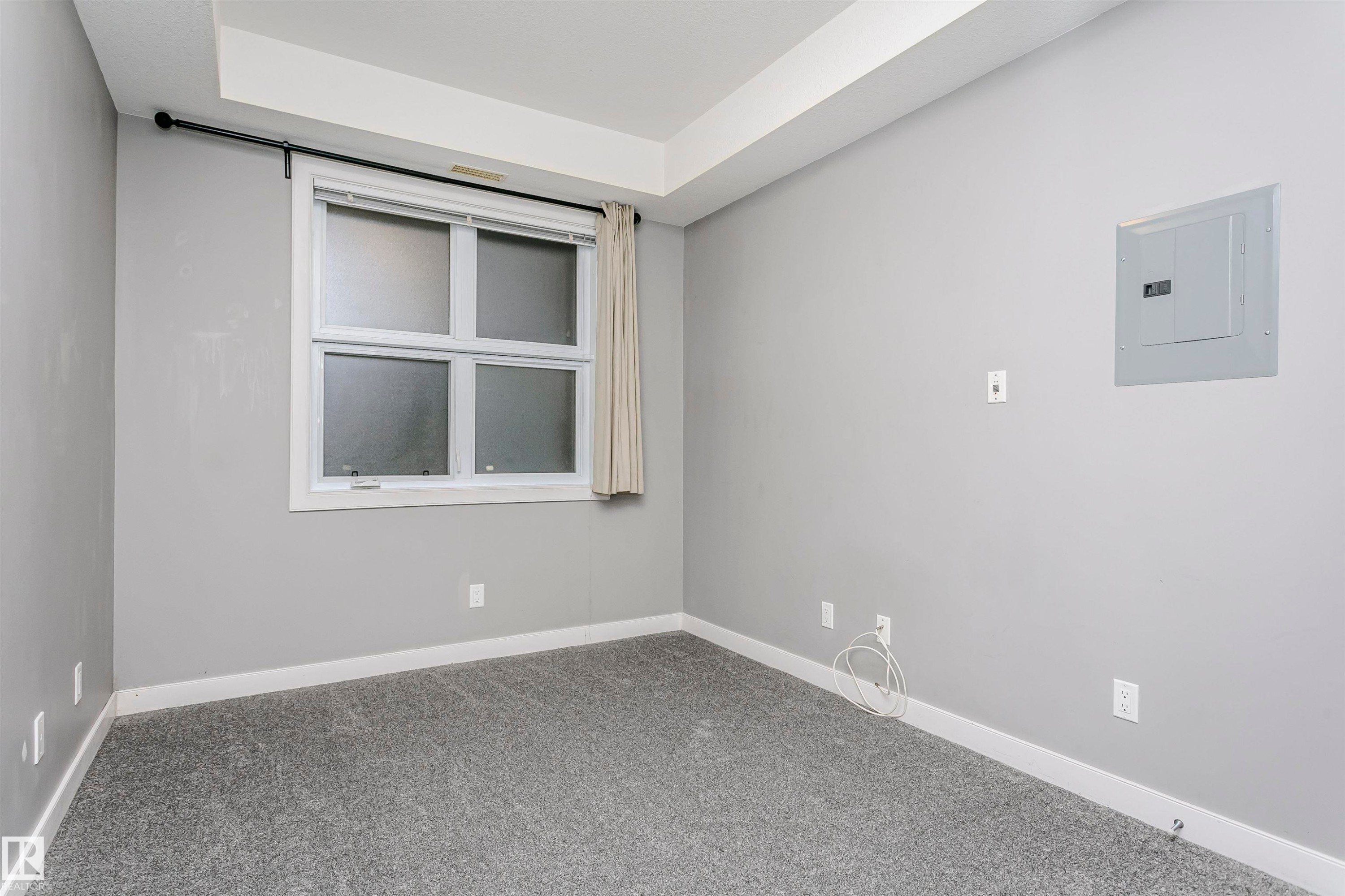 Room featuring a frosted pane window with white trim, light gray wall paint, gray carpet flooring, white baseboards, and a tray ceiling detail - 211 10808 71 Avenue, Edmonton, AB