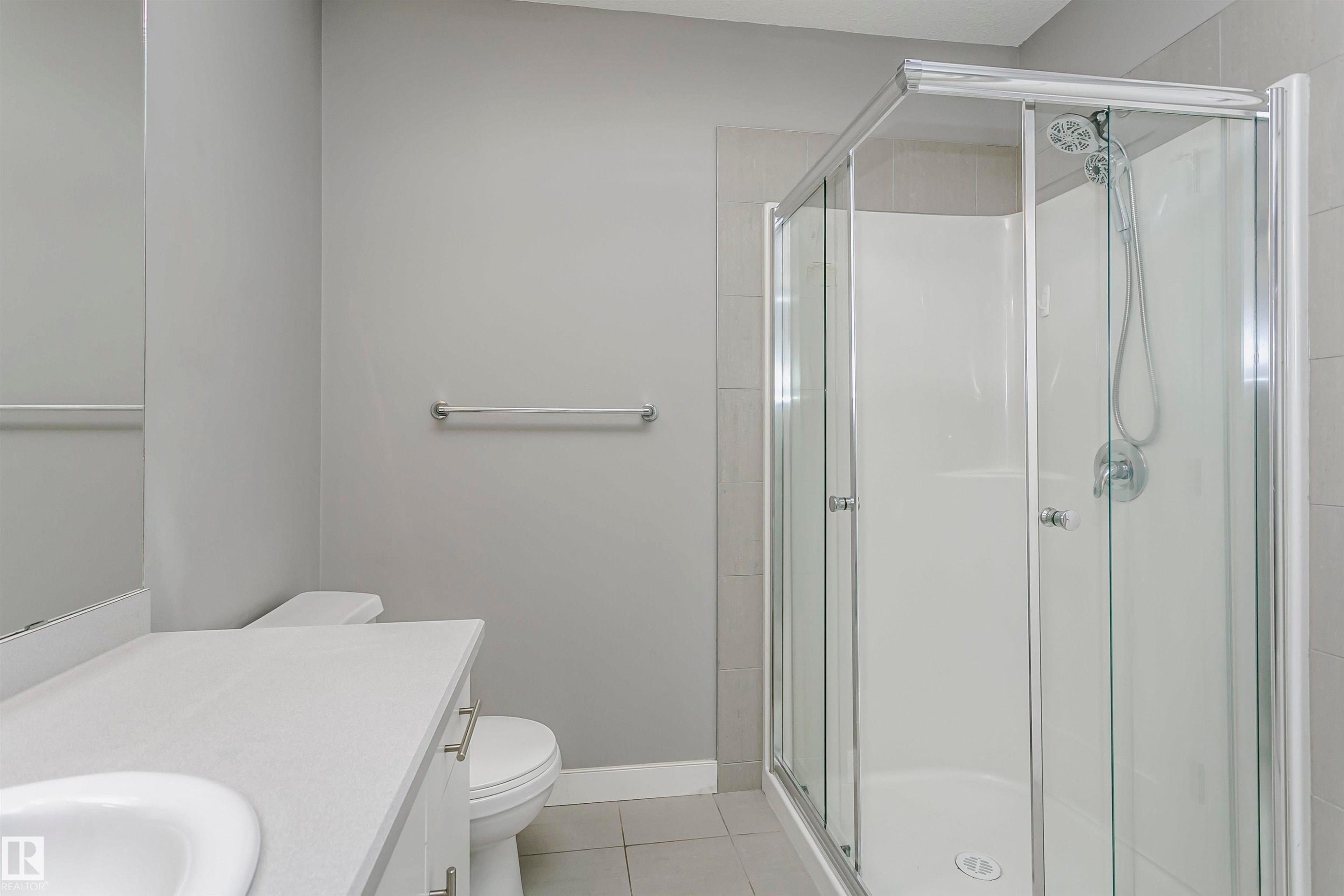 Corner glass-enclosed shower with white surround, complemented by a white vanity with an integrated sink and base cabinetry - 211 10808 71 Avenue, Edmonton, AB