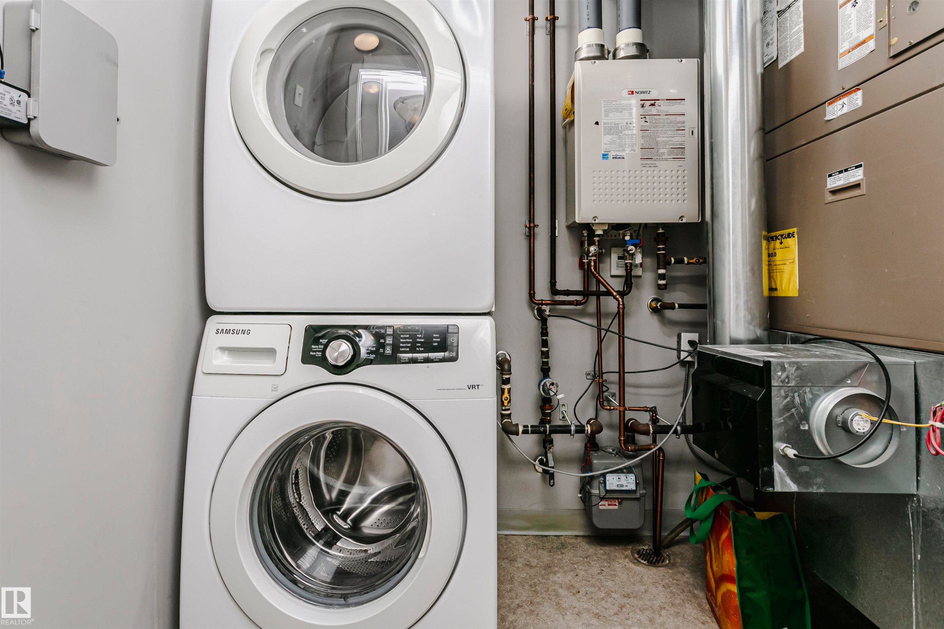 Dedicated utility area featuring a stacked washer and dryer unit, wall-mounted tankless water heater, and a furnace - 211 10808 71 Avenue, Edmonton, AB