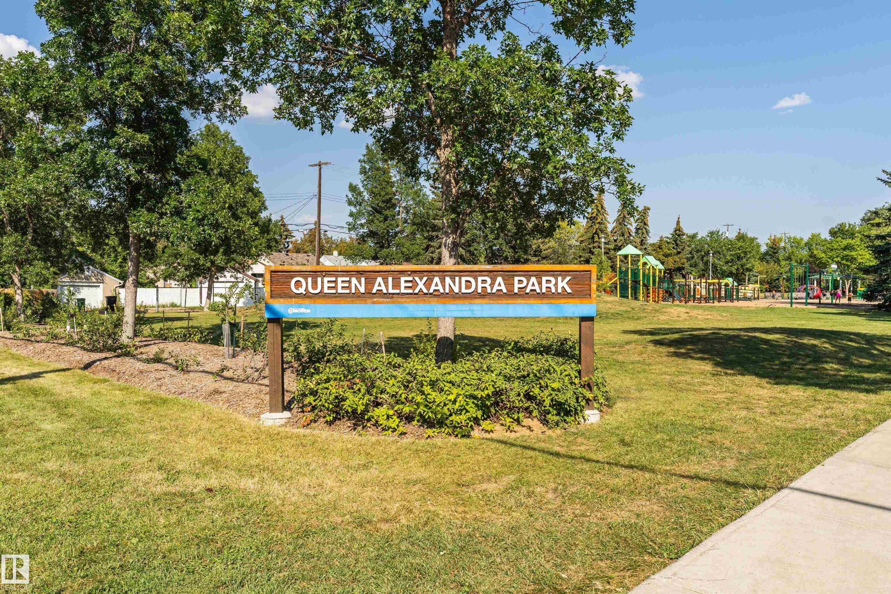 Park entrance featuring a wooden park sign, green space, and mature trees - 211 10808 71 Avenue, Edmonton, AB