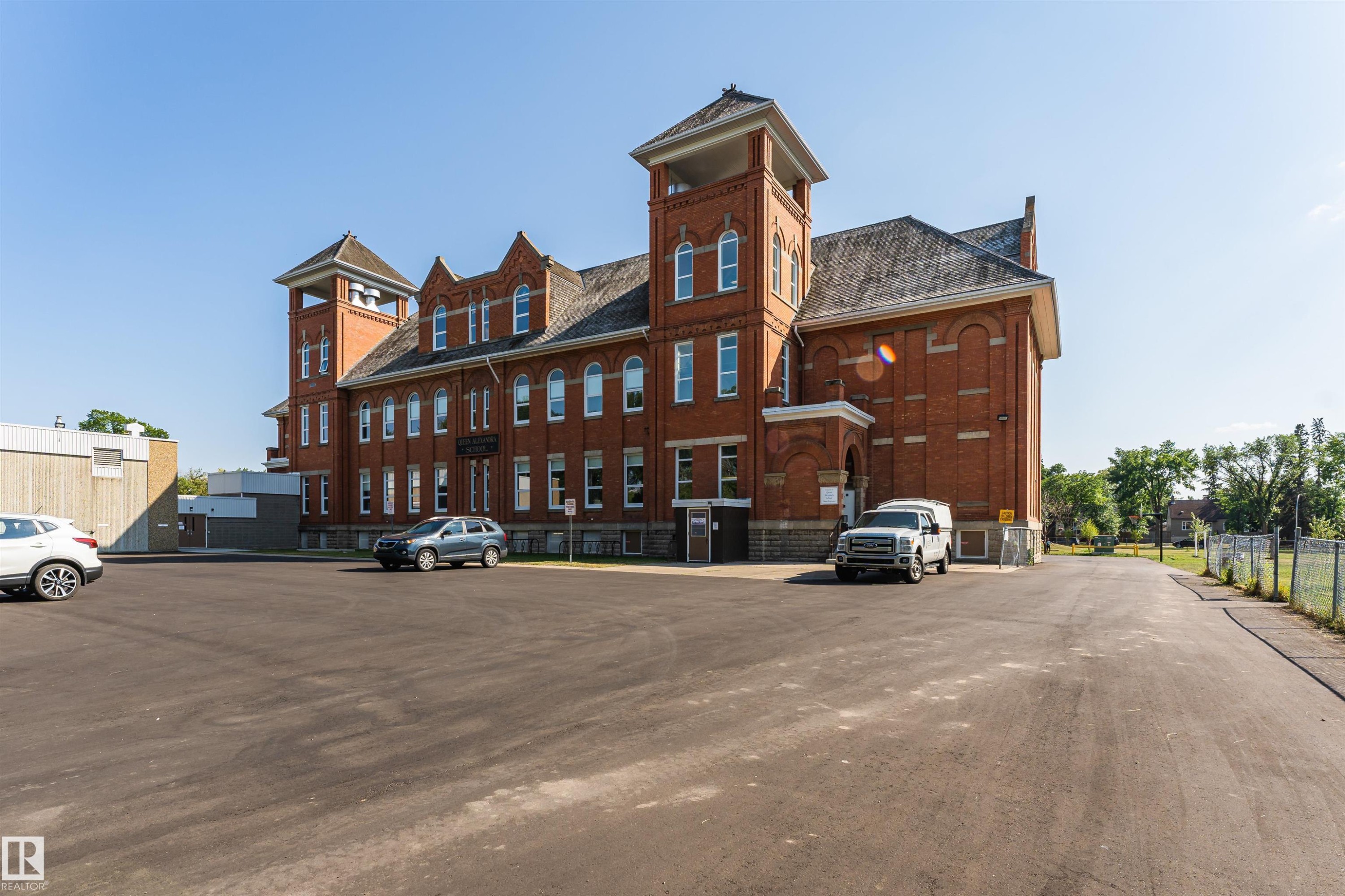 Historic red brick building featuring two prominent towers, multiple windows, and an arched entry - 211 10808 71 Avenue, Edmonton, AB