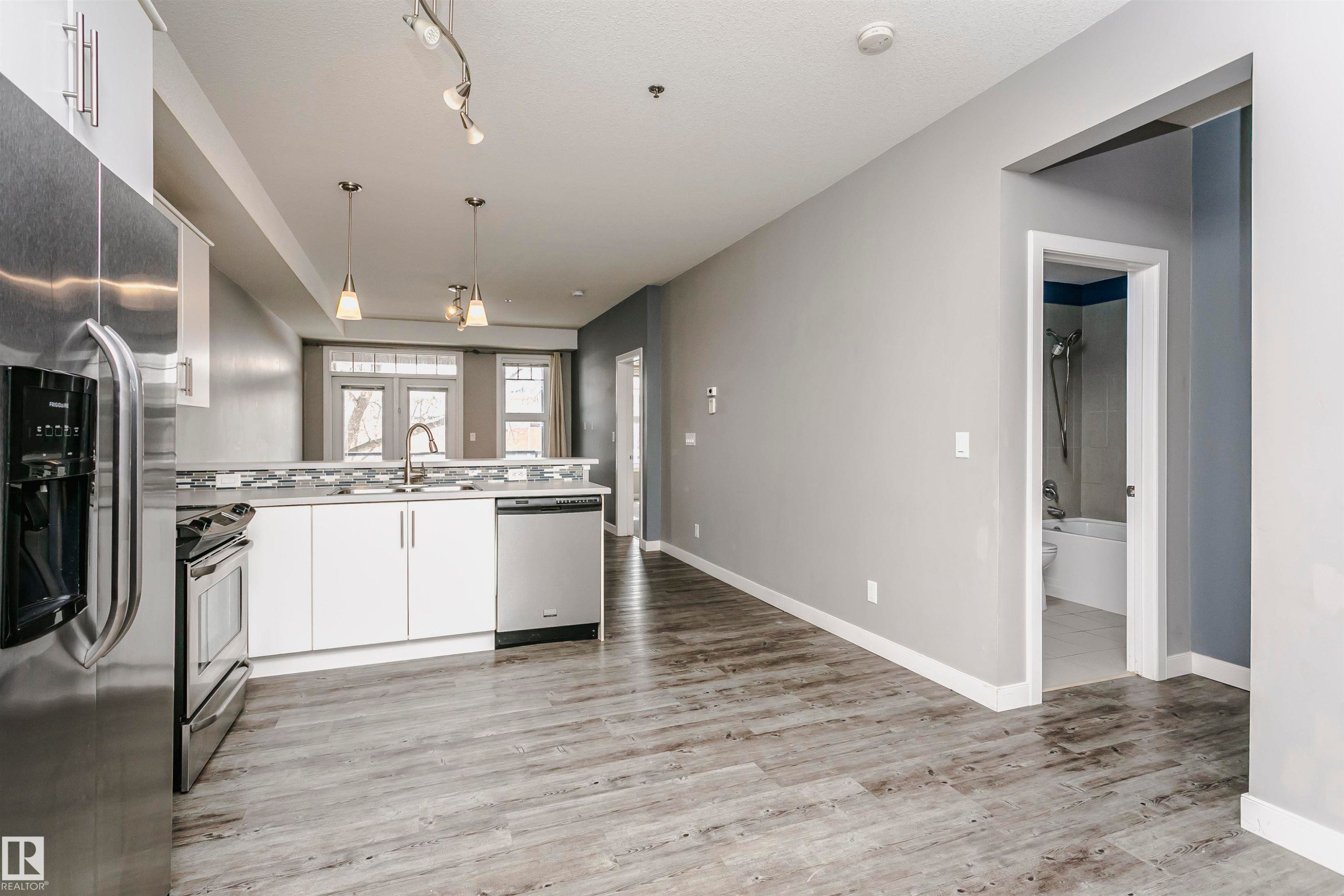 Modern kitchen featuring stainless steel appliances, white cabinetry, a tile backsplash, and pendant lighting - 211 10808 71 Avenue, Edmonton, AB