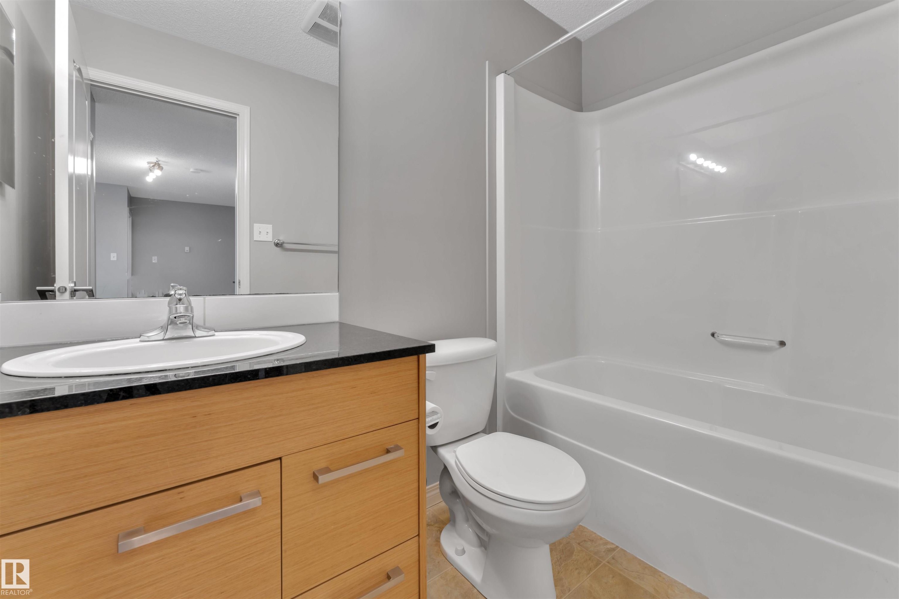 Bathroom featuring a wood-finish vanity with a built-in sink, a dark countertop, a mirror, and a combined shower and tub unit - #3302 9351 Simpson Dr Nw, Edmonton, AB