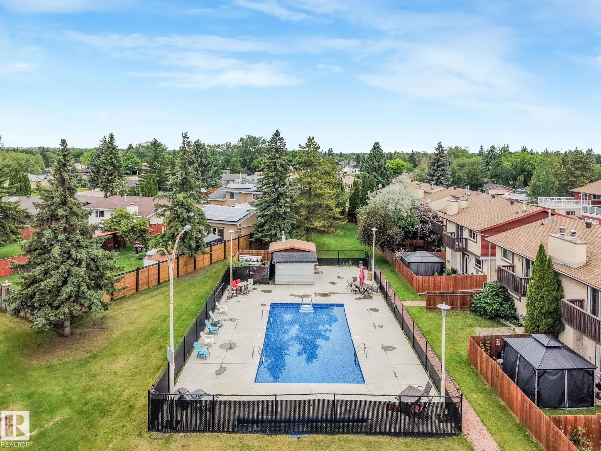Private outdoor swimming pool with surrounding concrete deck, black metal fencing, and a small pool house - 2921 130 Avenue, Edmonton, AB