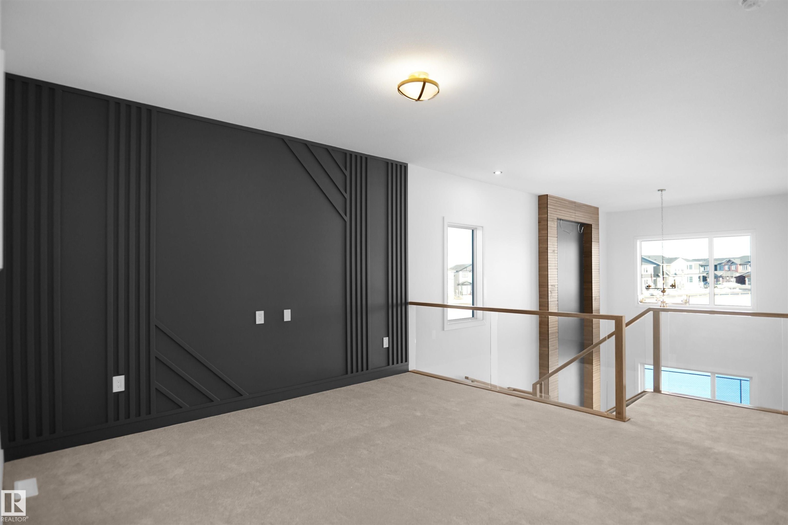 Accent wall featuring geometric paneling, plush carpeting, modern ceiling light fixture, expansive windows, and glass railing with wood-finish top - 6403 29 Ave, Edmonton, AB - Indoor Photo Showing Other Room