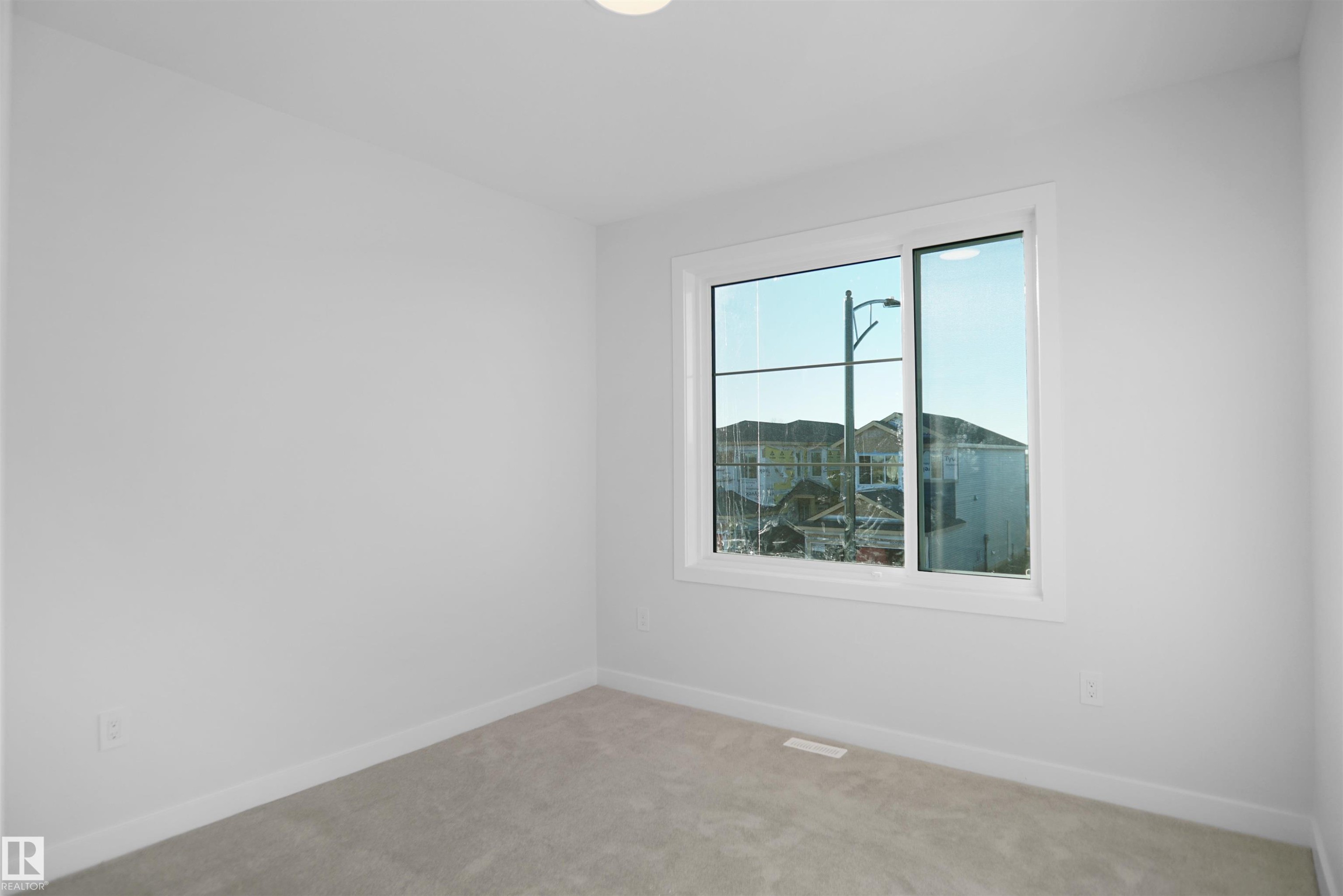Bright interior space featuring a window with white trim, light gray carpet, white baseboards, and a flush-mount ceiling light - 6403 29 Ave, Edmonton, AB - Indoor Photo Showing Other Room