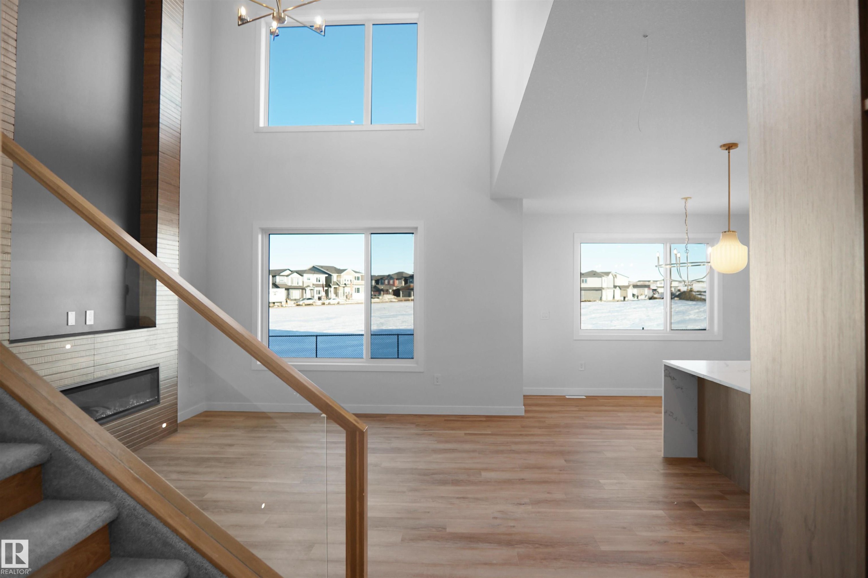 Two-story living room featuring a wood-panel accent wall with built-in media console and linear fireplace, soaring ceilings, and multiple windows - 6403 29 Ave, Edmonton, AB - Indoor Photo Showing Other Room With Fireplace