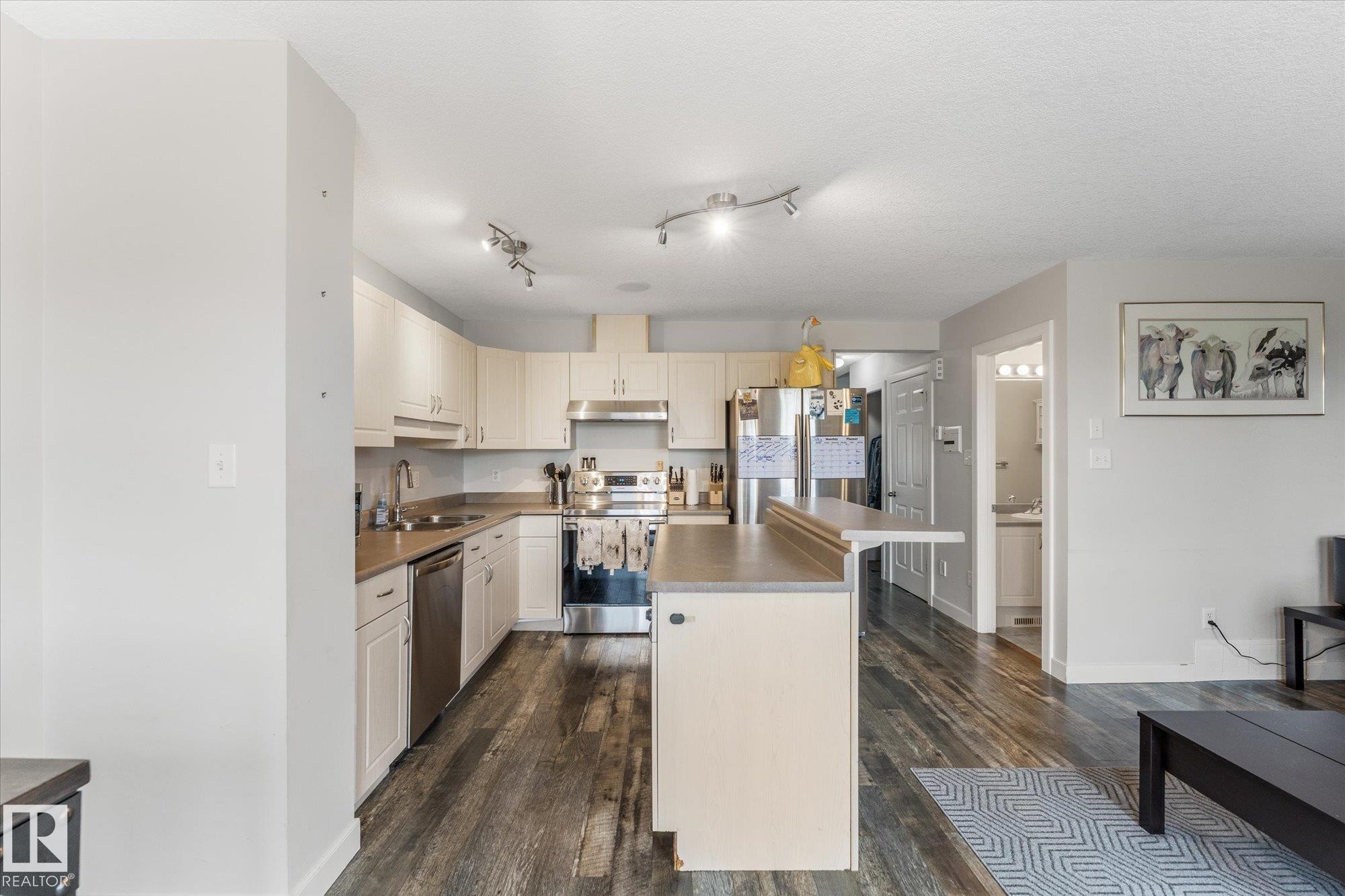 Kitchen featuring cream cabinetry, stainless steel appliances, a kitchen island with seating, dark wood-finish flooring, and recessed lighting - 2324 30 Avenue, Edmonton, AB