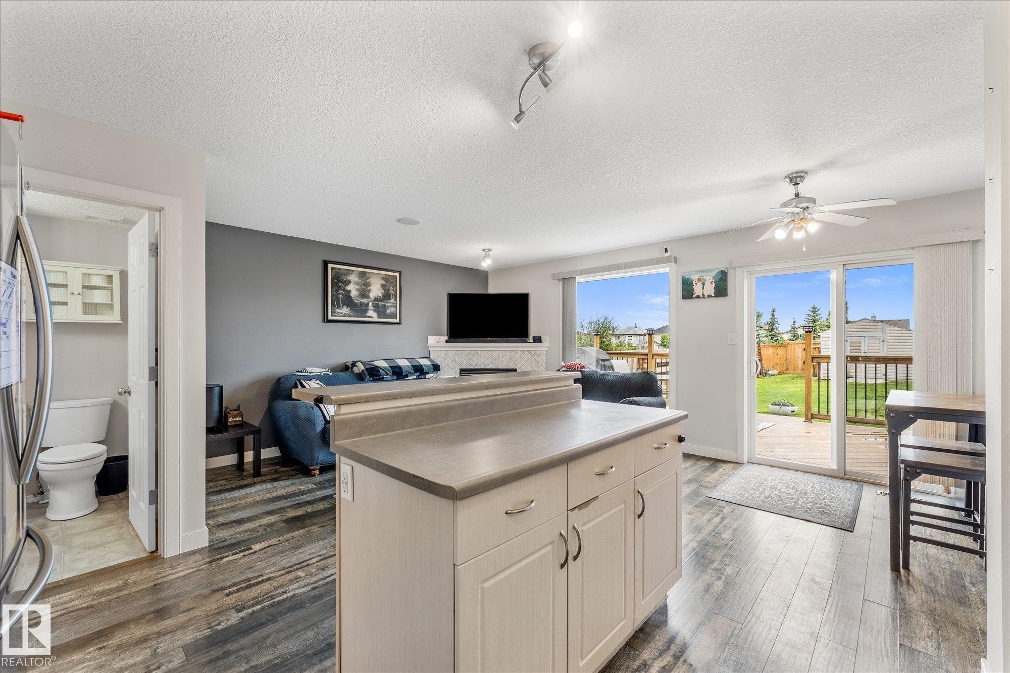 Open-concept living space featuring wood-finish flooring, a kitchen island with storage, and sliding glass doors leading to a wooden deck - 2324 30 Avenue, Edmonton, AB