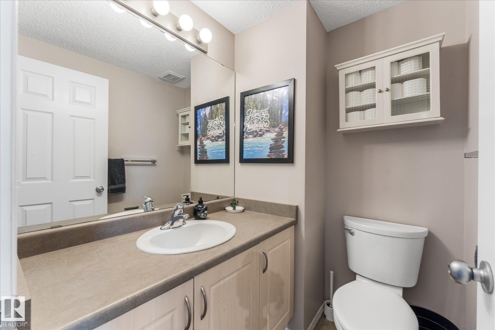 Bathroom featuring an integrated sink, vanity with under-sink storage, full wall mirror, and a wall-mounted light fixture - 2324 30 Avenue, Edmonton, AB