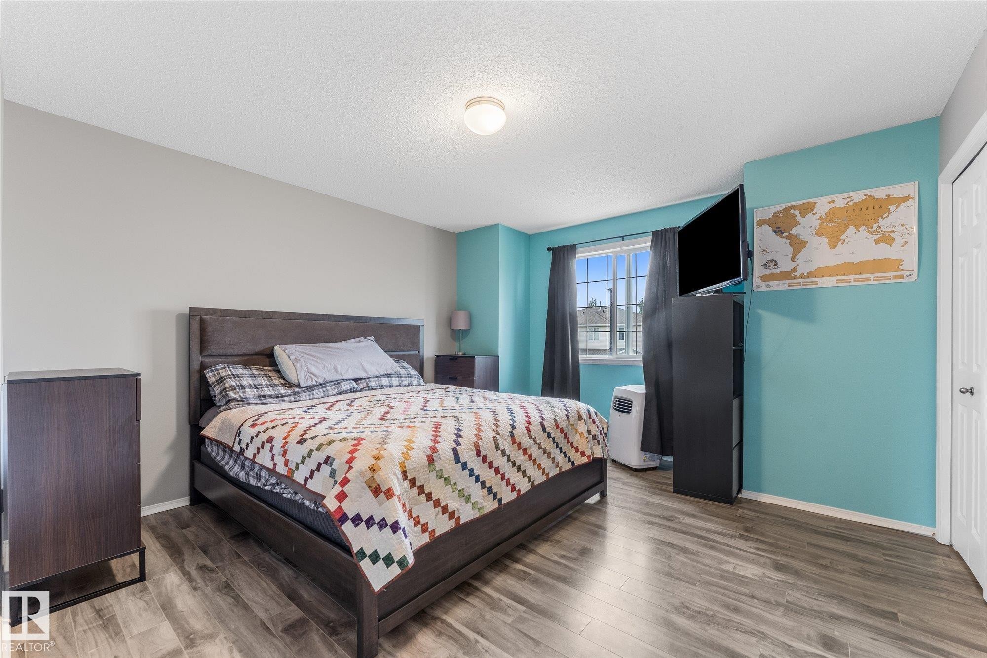 Spacious bedroom featuring wood-finish flooring, a contemporary ceiling light fixture, a window with vertical muntins, and a white paneled door - 2324 30 Avenue, Edmonton, AB