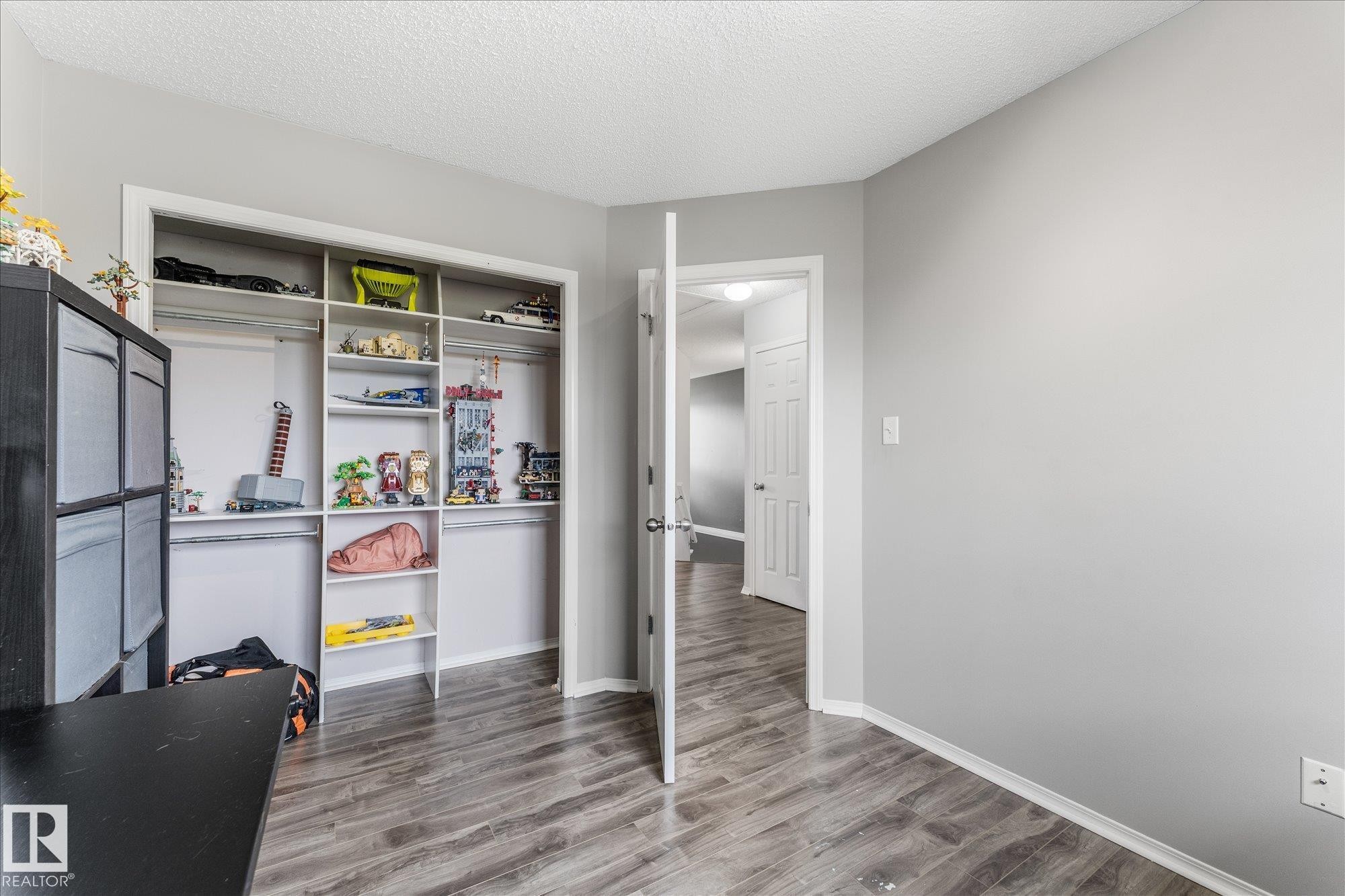 Neutral gray walls with white trim, wood-finish flooring, and a built-in closet organization system featuring shelving and hanging rods - 2324 30 Avenue, Edmonton, AB