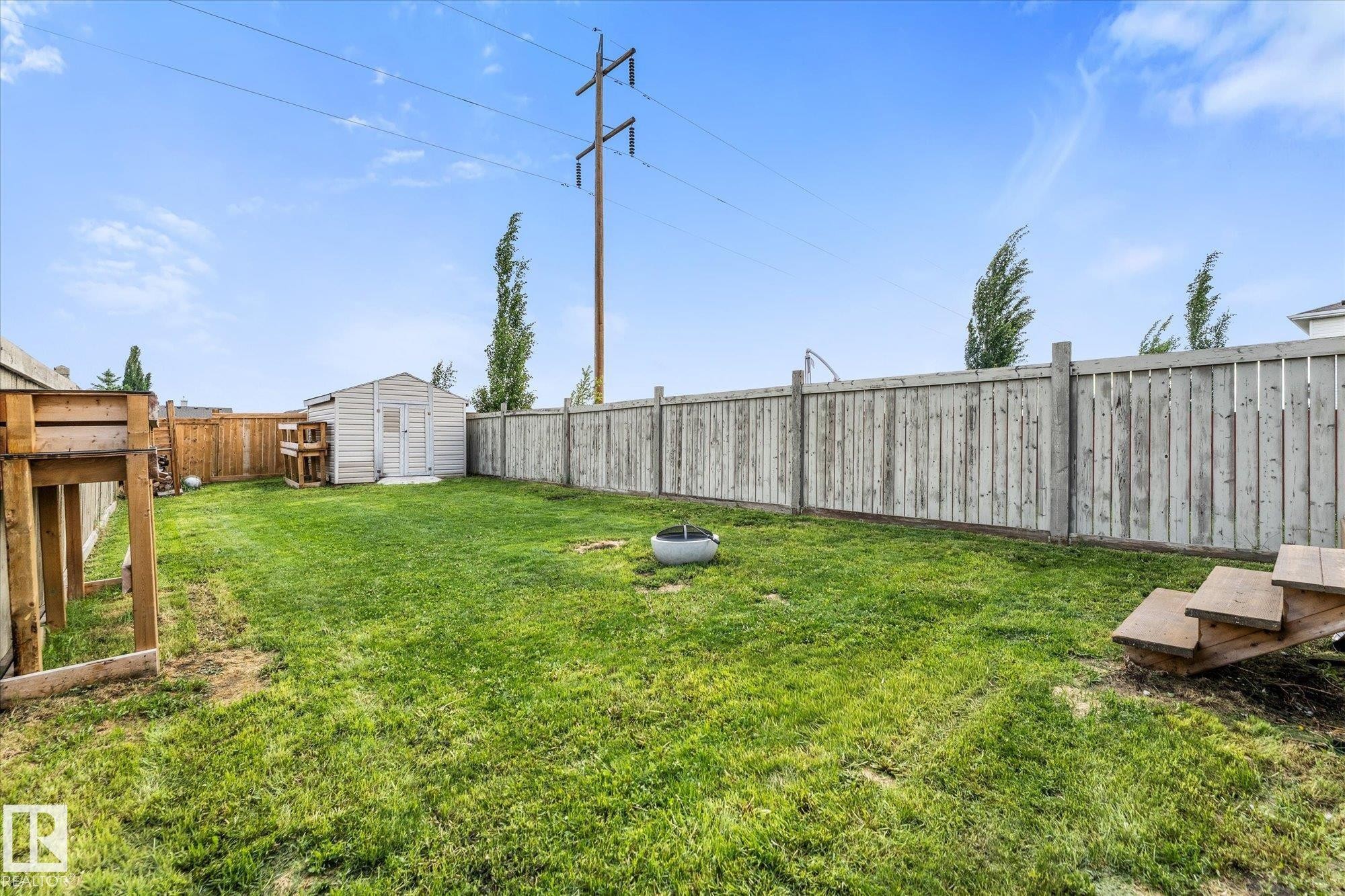 Spacious grass yard featuring a wooden privacy fence, a storage shed, and a circular fire pit - 2324 30 Avenue, Edmonton, AB