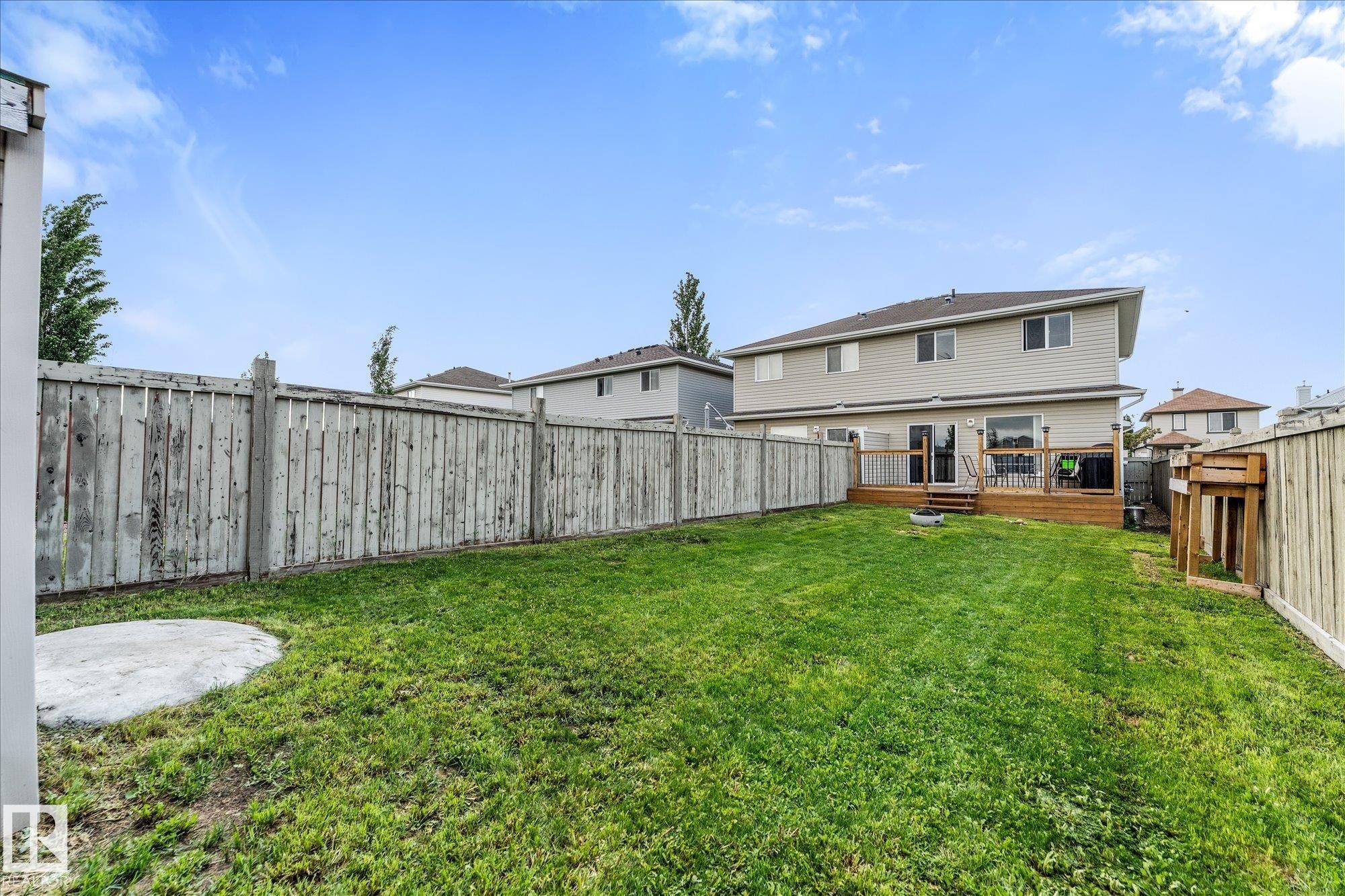 Expansive backyard featuring a wood deck, green lawn, full perimeter fencing, and a concrete pad - 2324 30 Avenue, Edmonton, AB