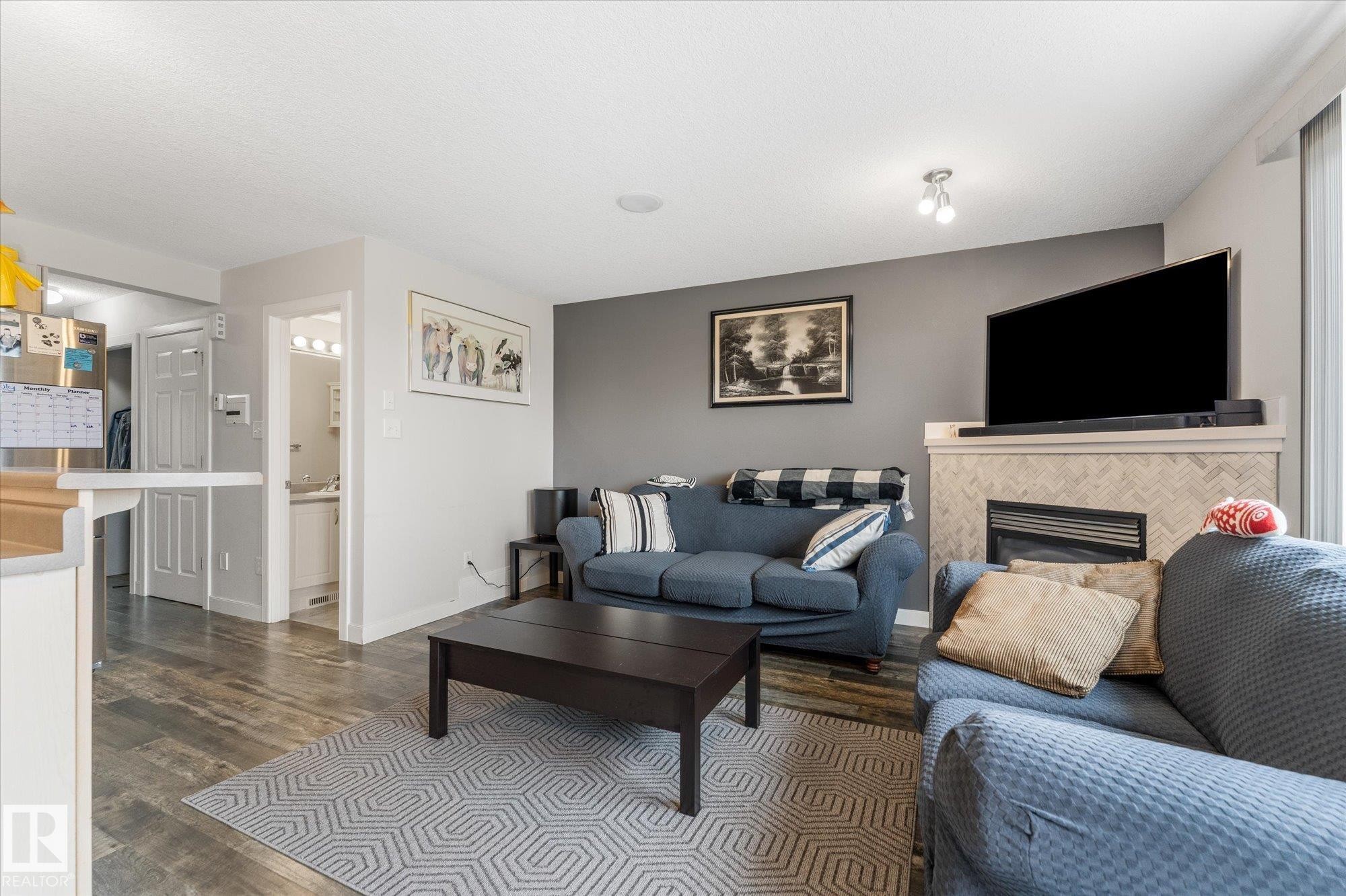 Living area featuring wood-finish flooring, a contemporary fireplace with a herringbone tile surround, and a mantel - 2324 30 Avenue, Edmonton, AB