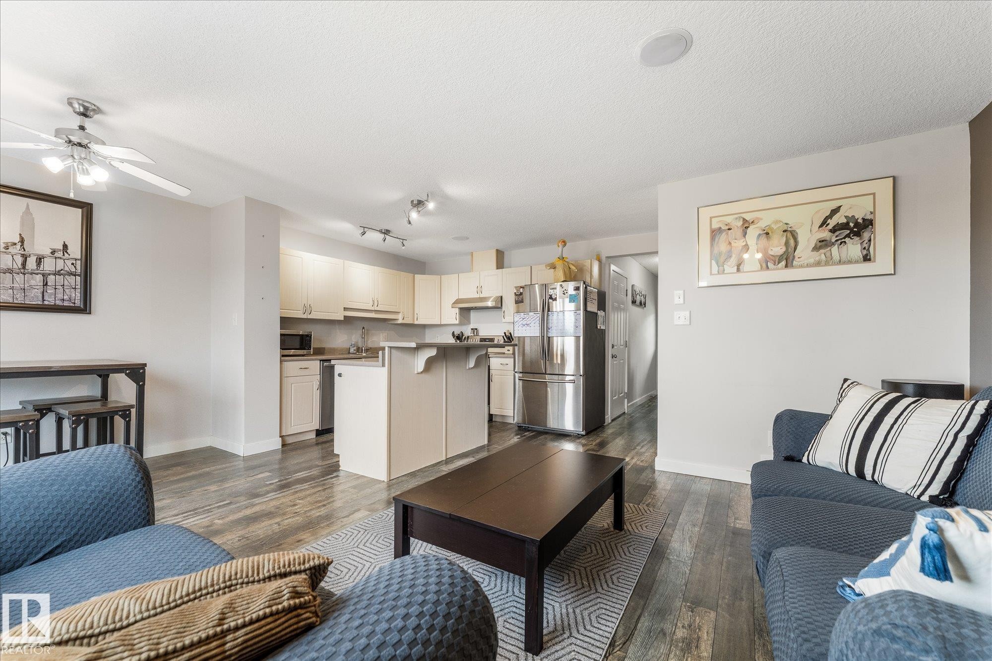 Open-concept living space featuring wood-finish flooring, a kitchen with light-colored cabinetry and stainless steel appliances, a kitchen island with seating, a ceiling fan, and recessed lighting - 2324 30 Avenue, Edmonton, AB
