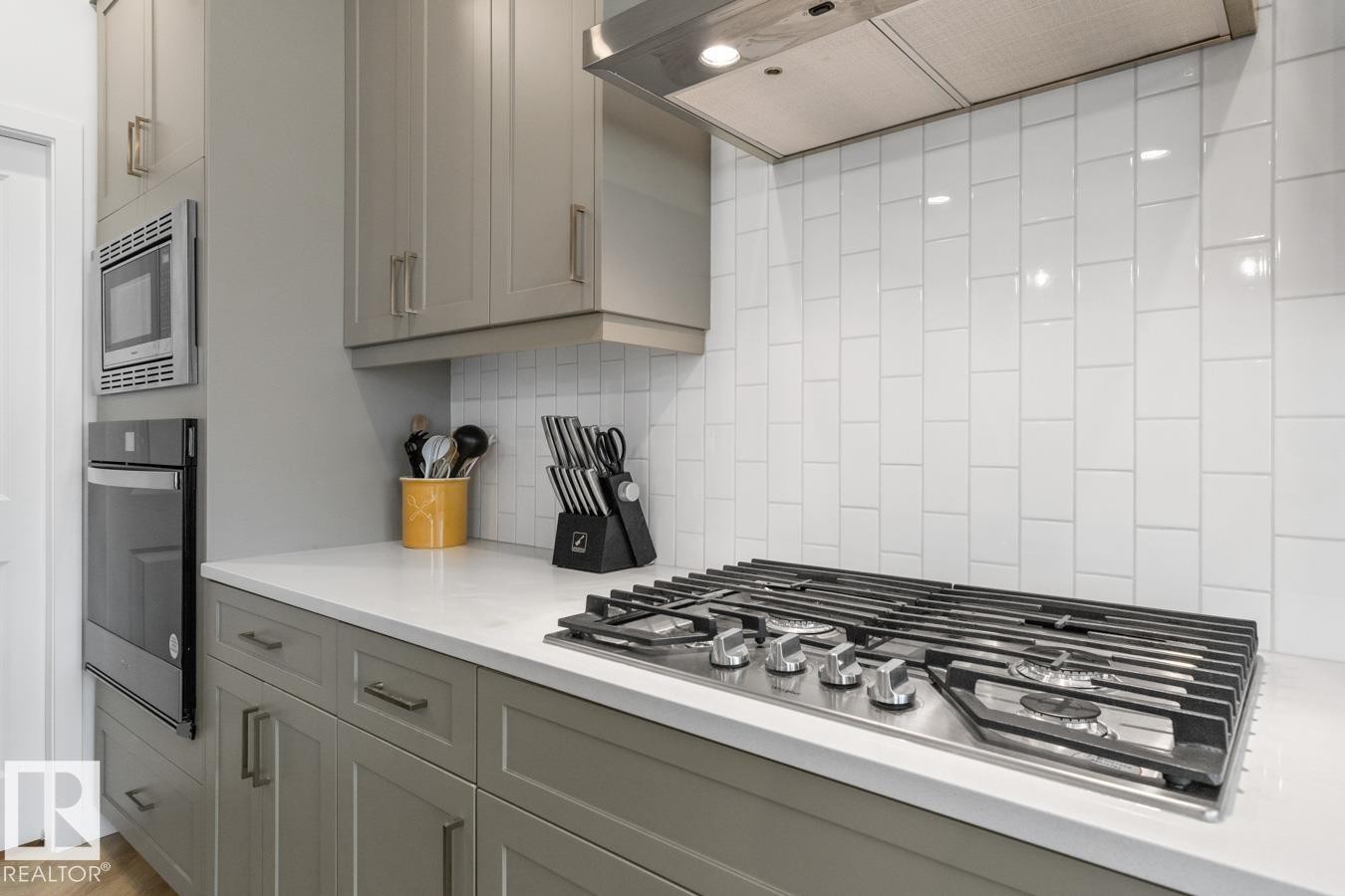 Kitchen featuring a built-in gas range, white subway tile backsplash, and light gray cabinetry - 117 Paisley Gate Gate, Edmonton, AB