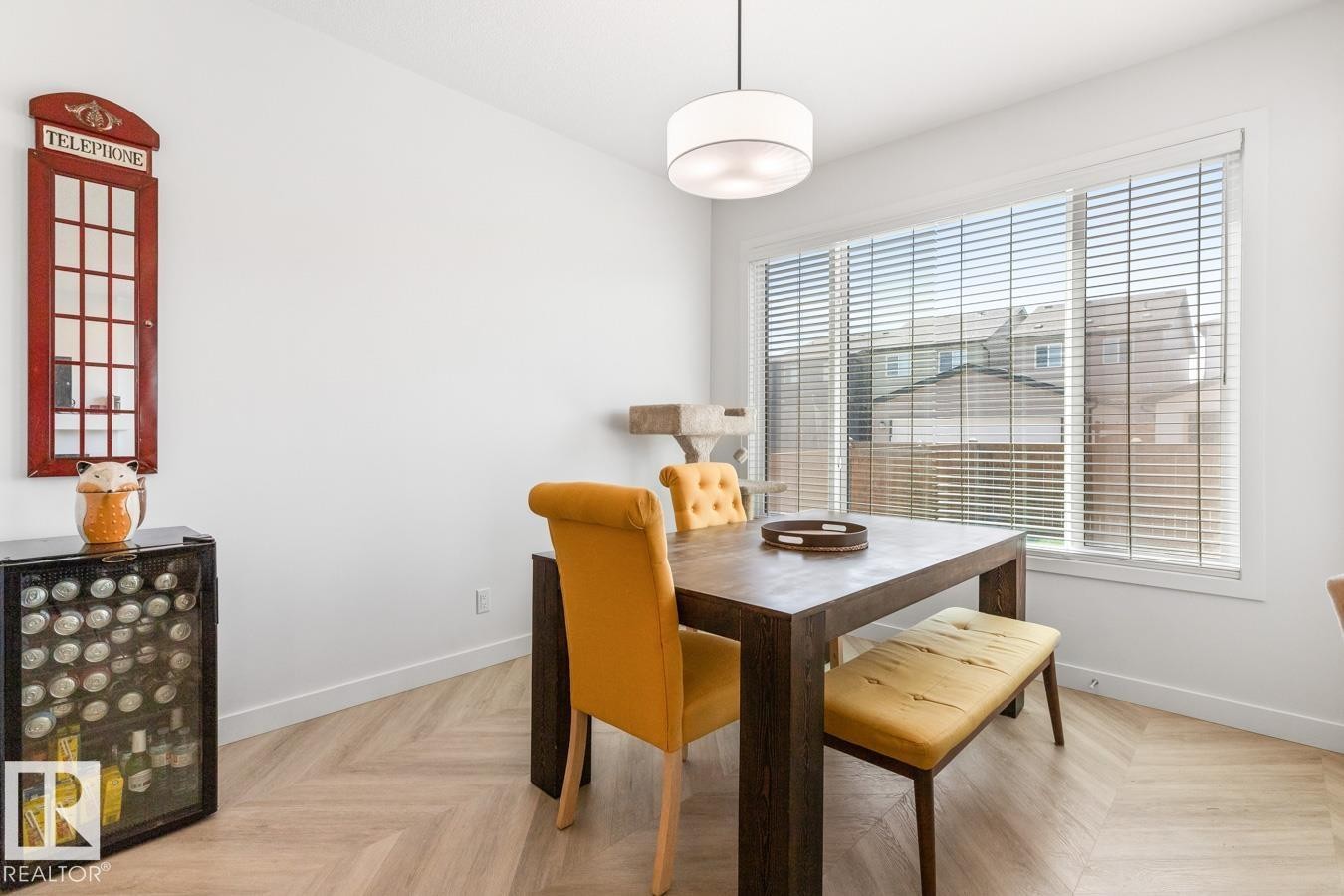 Spacious room featuring a large window with horizontal blinds, light wood-finish flooring in a herringbone pattern, a contemporary ceiling light fixture, and white painted walls - 117 Paisley Gate Gate, Edmonton, AB