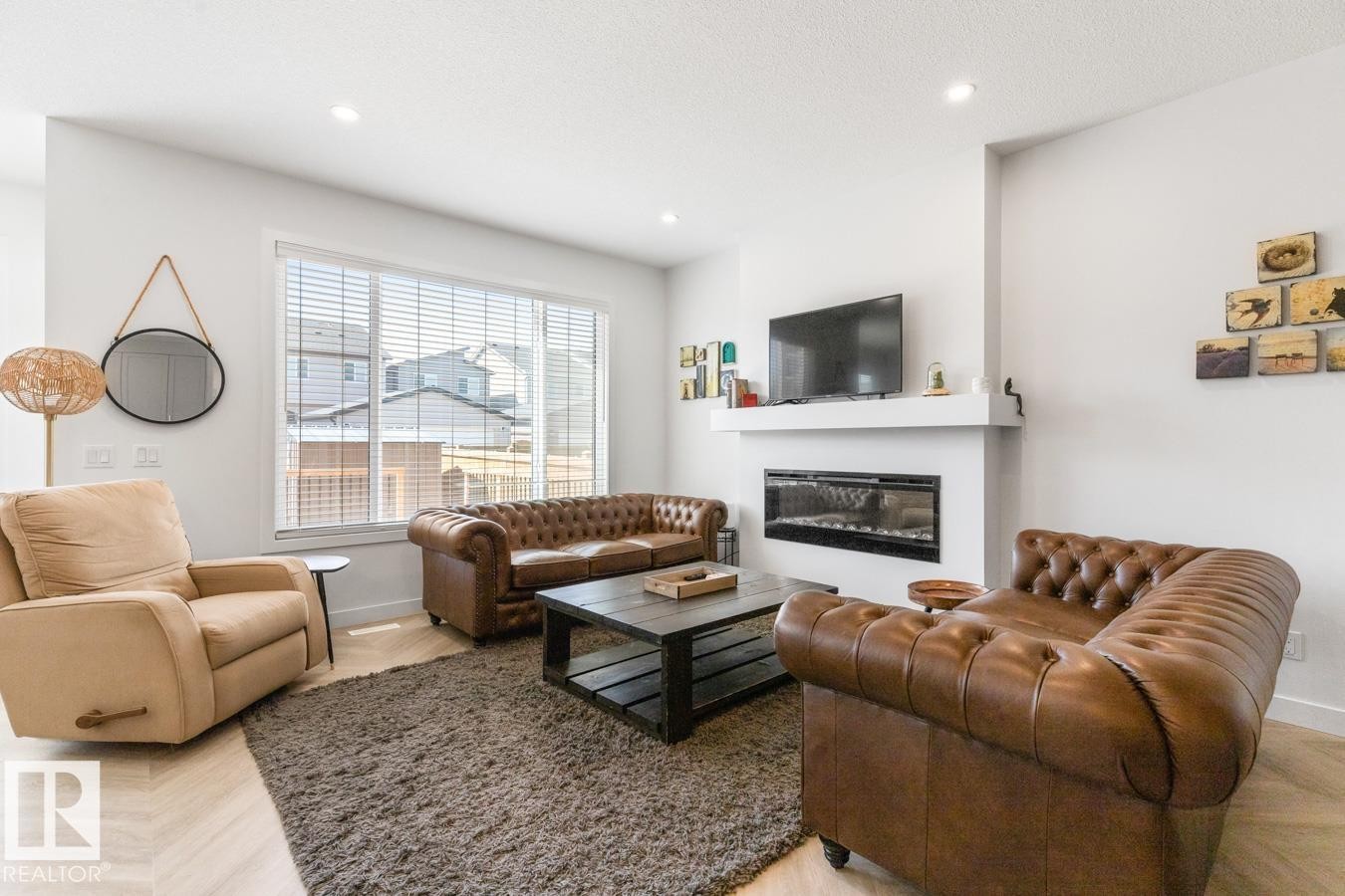 Living area featuring a sleek linear fireplace with a white mantel, large windows with blinds, and light wood-finish flooring - 117 Paisley Gate Gate, Edmonton, AB