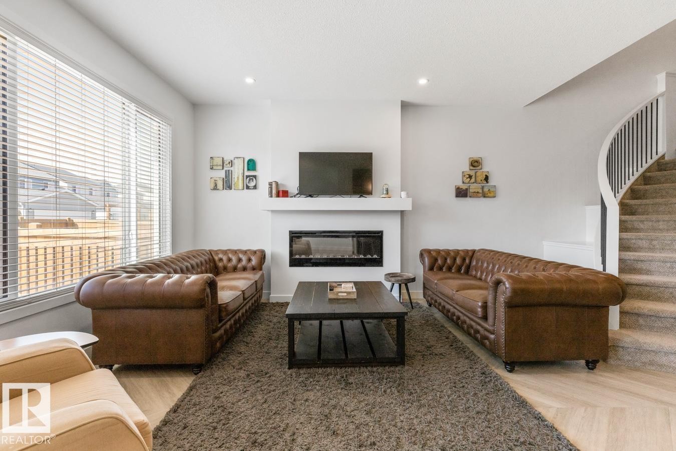 Contemporary living area featuring a built-in fireplace, light wood-finish flooring, and a curved staircase with black metal balusters - 117 Paisley Gate Gate, Edmonton, AB