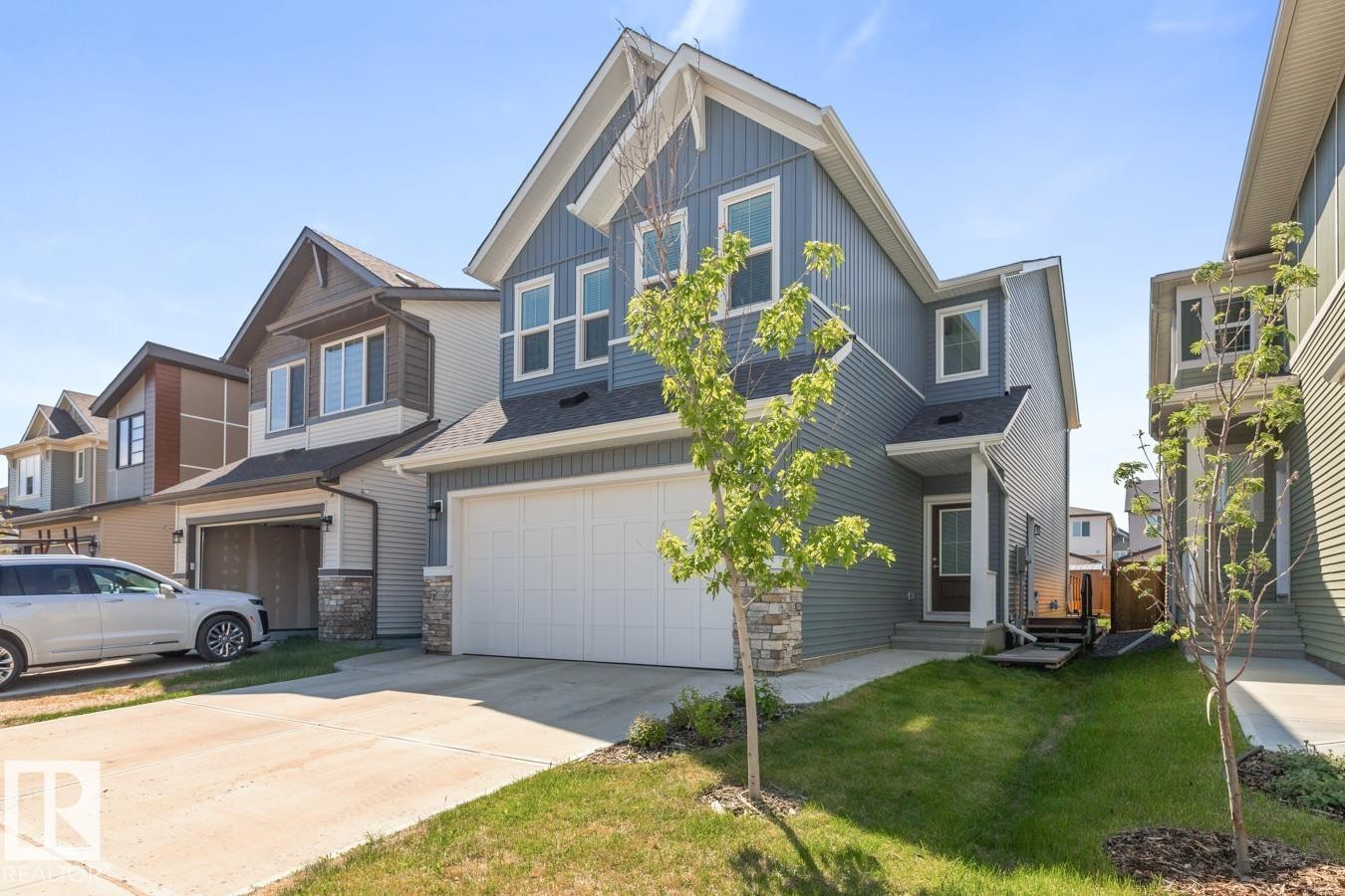 Contemporary two-story residence featuring blue horizontal siding, white trim, a stone accent column, and an attached two-car garage - 117 Paisley Gate Gate, Edmonton, AB