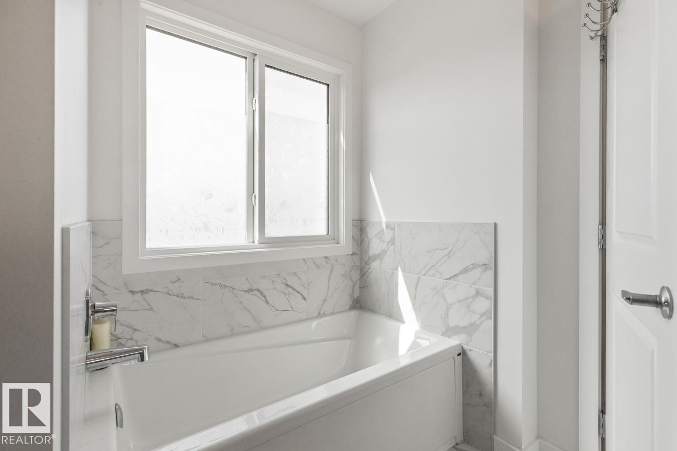 Soaking tub featuring chrome fixtures and white marble-look tile surround - 117 Paisley Gate Gate, Edmonton, AB