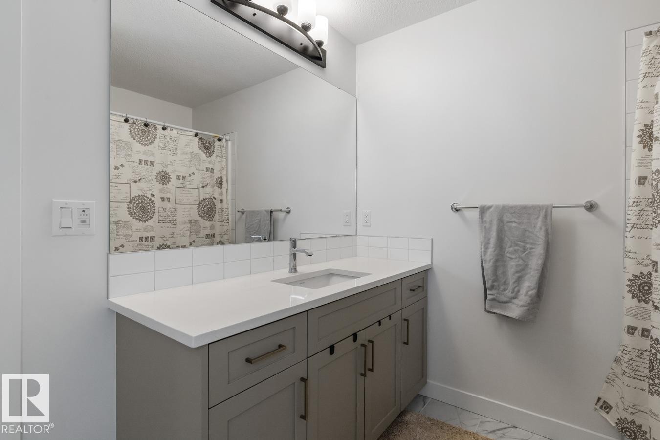 Bathroom featuring a large vanity with gray cabinetry and brushed nickel hardware, a white countertop with an integrated sink, and a chrome faucet - 117 Paisley Gate Gate, Edmonton, AB