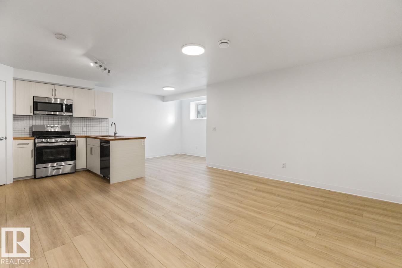 Open-concept living space featuring a kitchen with stainless steel appliances, white cabinetry, a tiled backsplash, and wood-finish flooring - 117 Paisley Gate Gate, Edmonton, AB