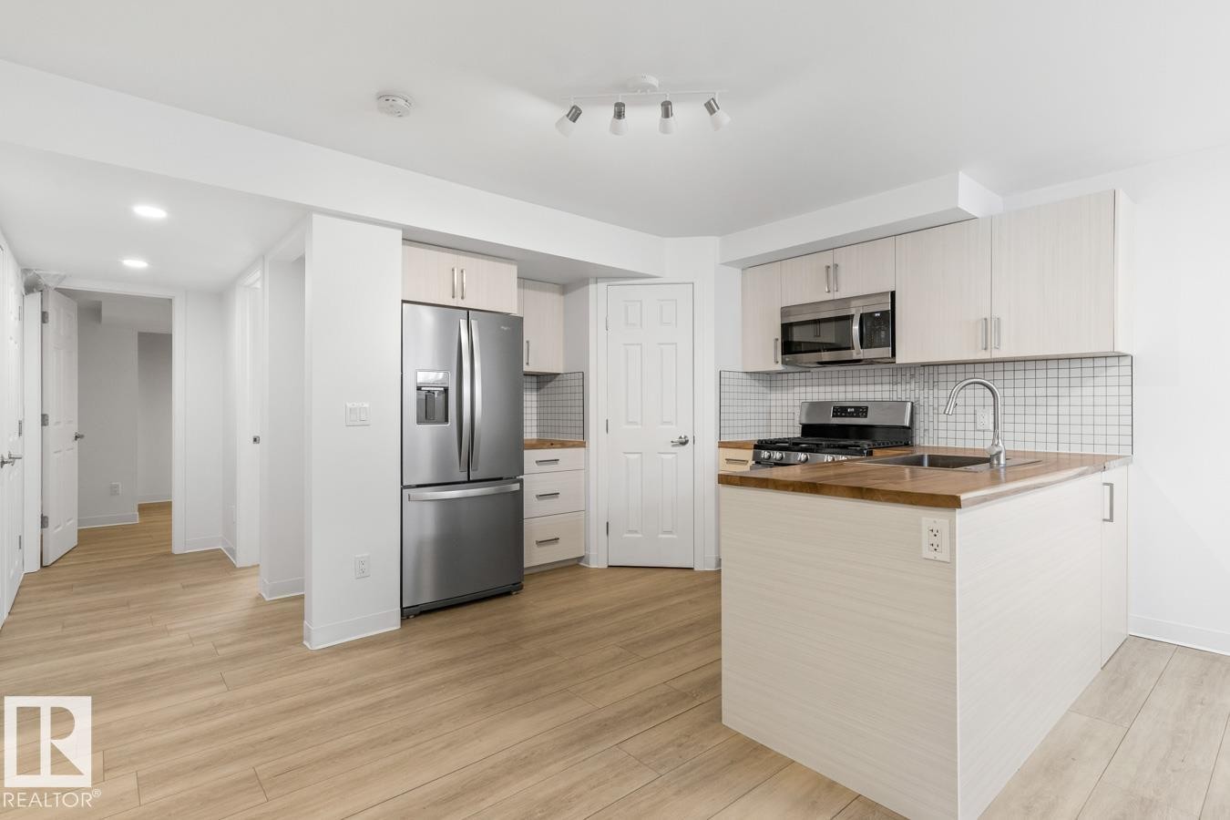Modern kitchen featuring light wood-finish flooring, stainless steel appliances, white cabinetry, a tiled backsplash, and natural wood countertops - 117 Paisley Gate Gate, Edmonton, AB