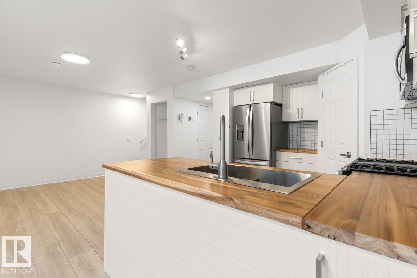 Modern kitchen island featuring a stainless steel sink with gooseneck faucet, butcher block countertops, and white cabinetry - 117 Paisley Gate Gate, Edmonton, AB