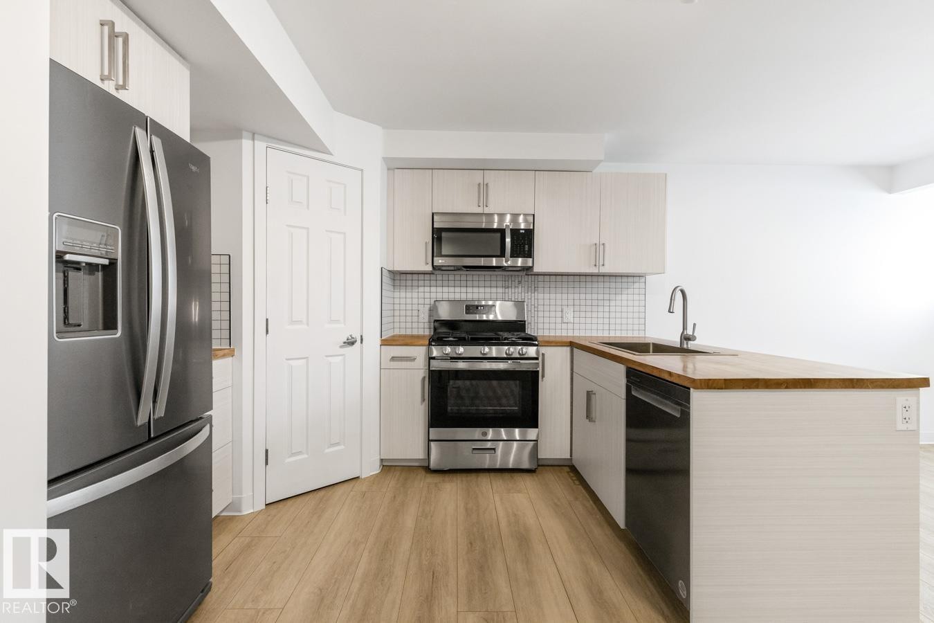 Modern kitchen featuring wood-finish flooring, light-toned cabinetry, stainless steel appliances, a white tile backsplash, and a wood-finish countertop with an integrated sink - 117 Paisley Gate Gate, Edmonton, AB