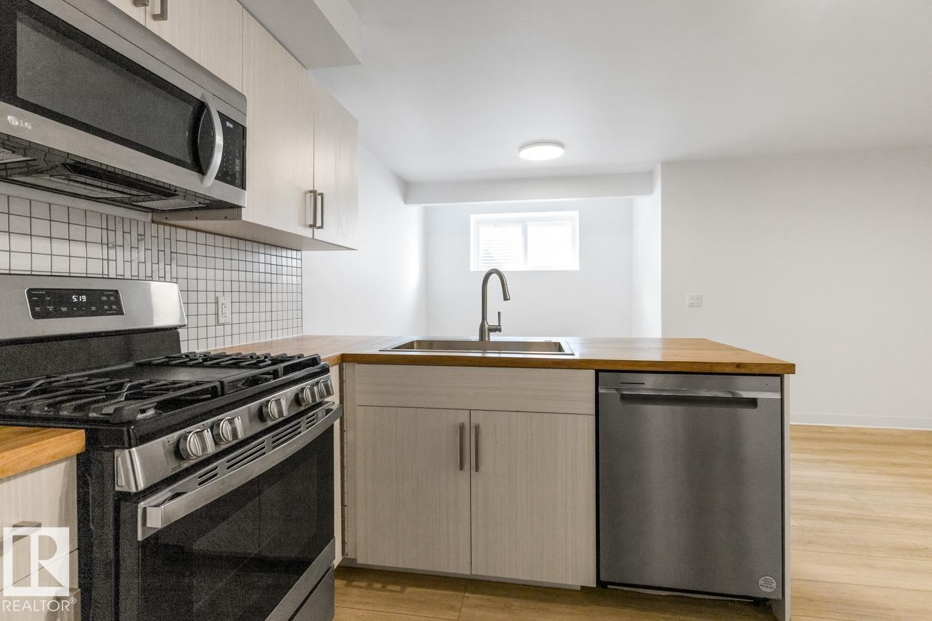 Modern kitchen featuring stainless steel appliances, light-toned wood-finish countertops, white shaker-style cabinetry, and a white square tile backsplash - 117 Paisley Gate Gate, Edmonton, AB