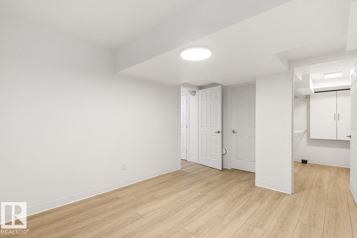 Spacious room featuring light wood-finish flooring, white walls, and a contemporary ceiling light fixture - 117 Paisley Gate Gate, Edmonton, AB