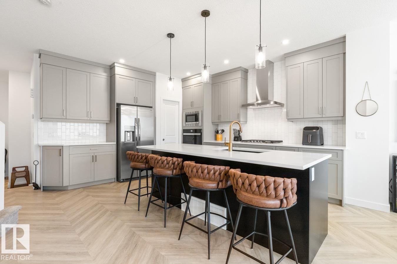 Contemporary kitchen featuring an oversized island with seating, light gray cabinetry, white subway tile backsplash, stainless steel appliances, and a gold-finish faucet - 117 Paisley Gate Gate, Edmonton, AB