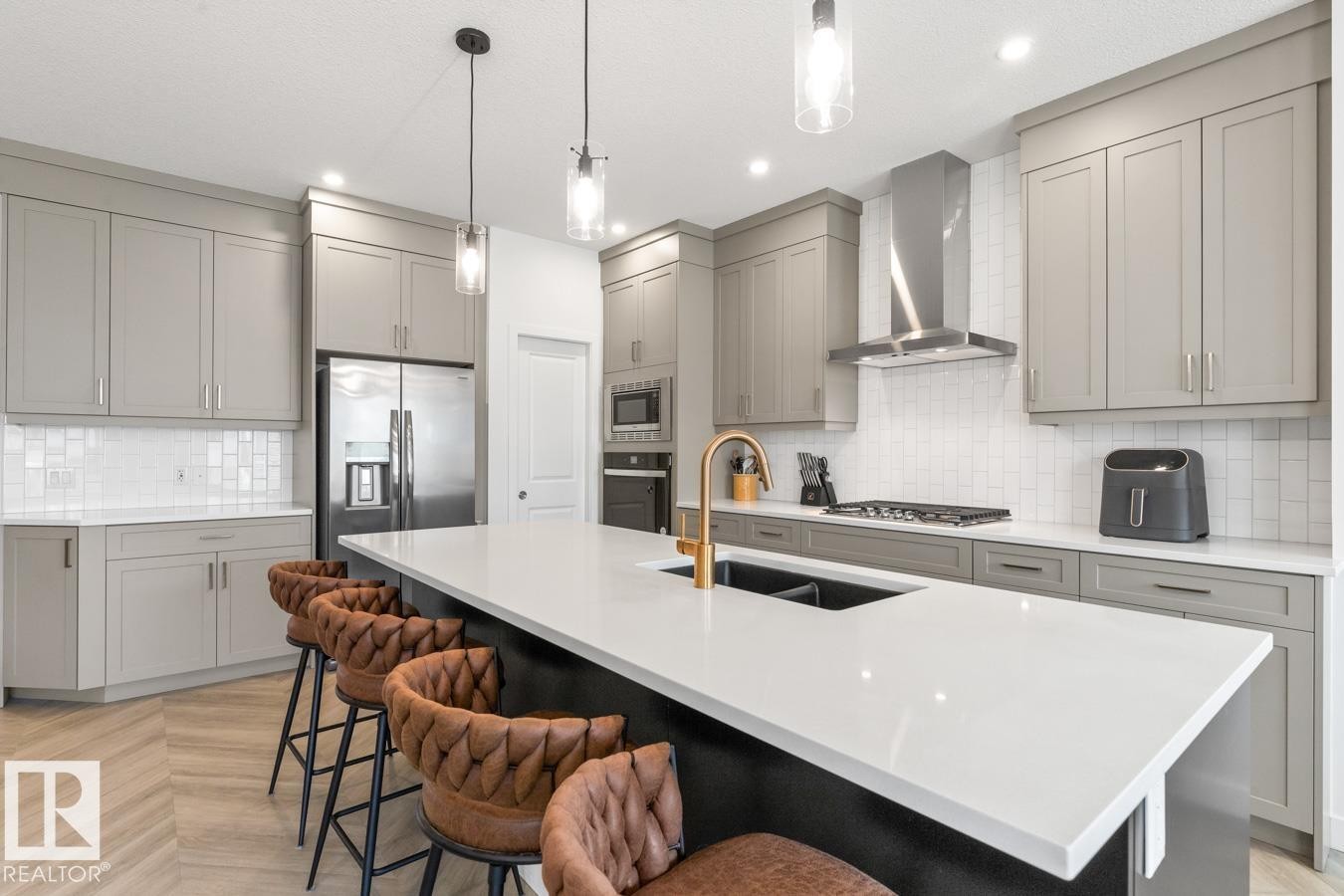 Spacious kitchen featuring an expansive island with white countertops, light gray cabinetry, stainless steel appliances, and wood-finish flooring - 117 Paisley Gate Gate, Edmonton, AB
