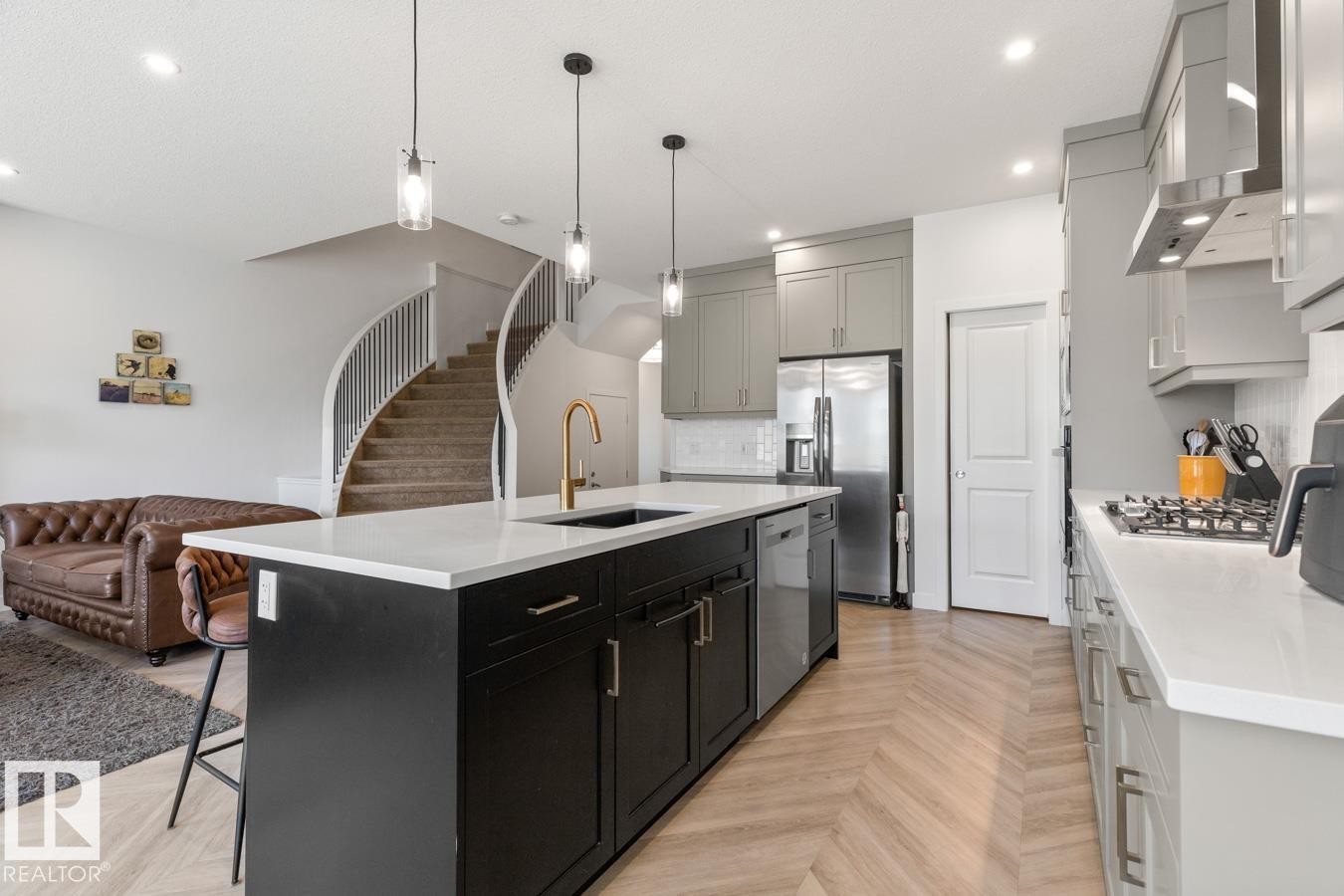 Kitchen featuring a large island with a gold-finish faucet, light gray perimeter cabinetry, stainless steel appliances, and herringbone pattern wood-finish flooring - 117 Paisley Gate Gate, Edmonton, AB