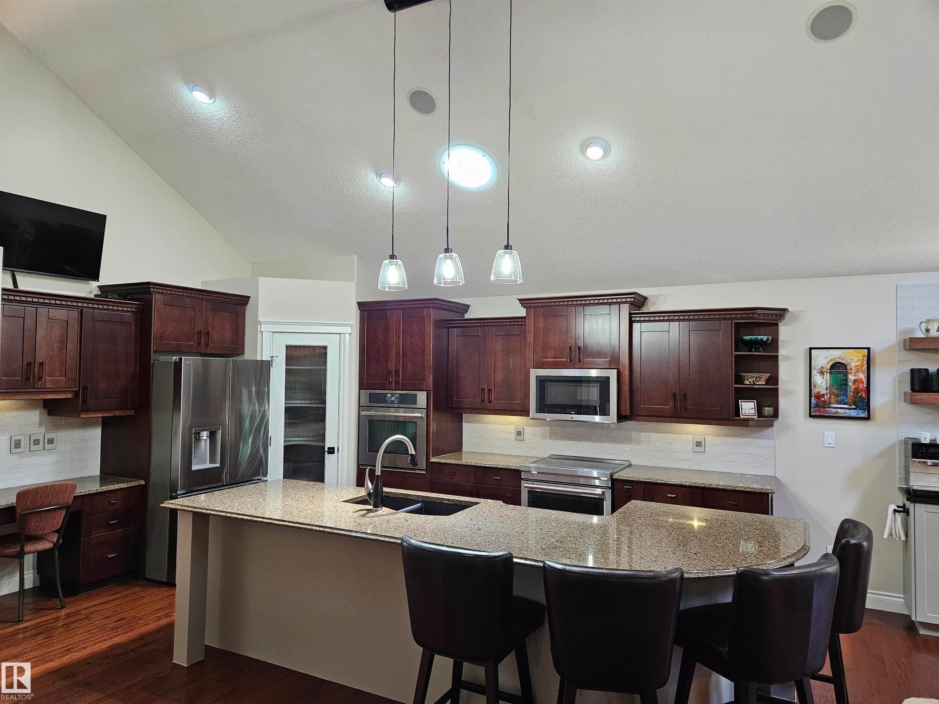 Gourmet kitchen featuring dark wood cabinetry, granite countertops, stainless steel appliances, and a central island with pendant lighting - 2322 Rutherford Way, Edmonton, AB