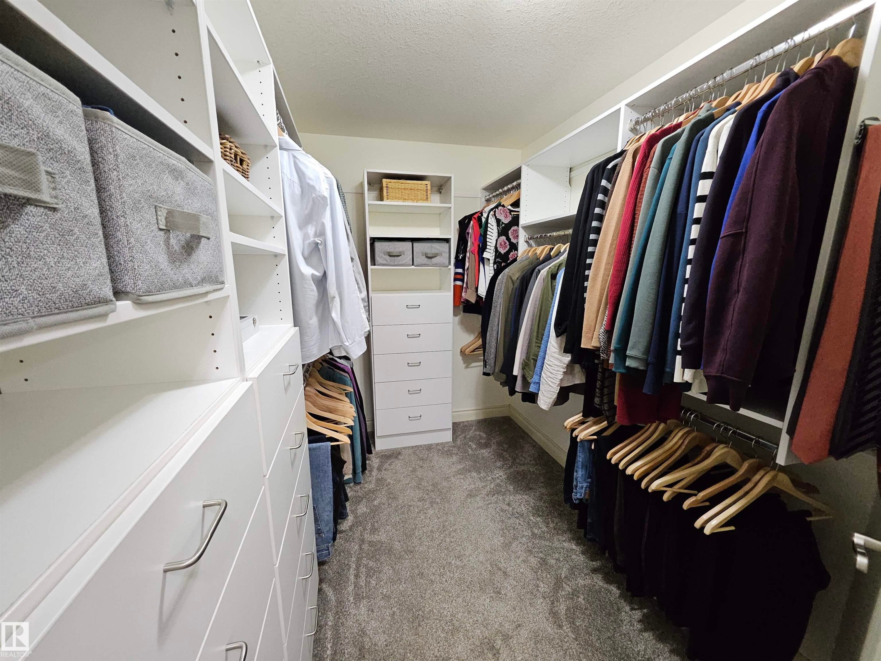 Custom closet system featuring multiple hanging rods, integrated shelving, built-in drawers with modern hardware, and soft gray carpeting - 2322 Rutherford Way, Edmonton, AB