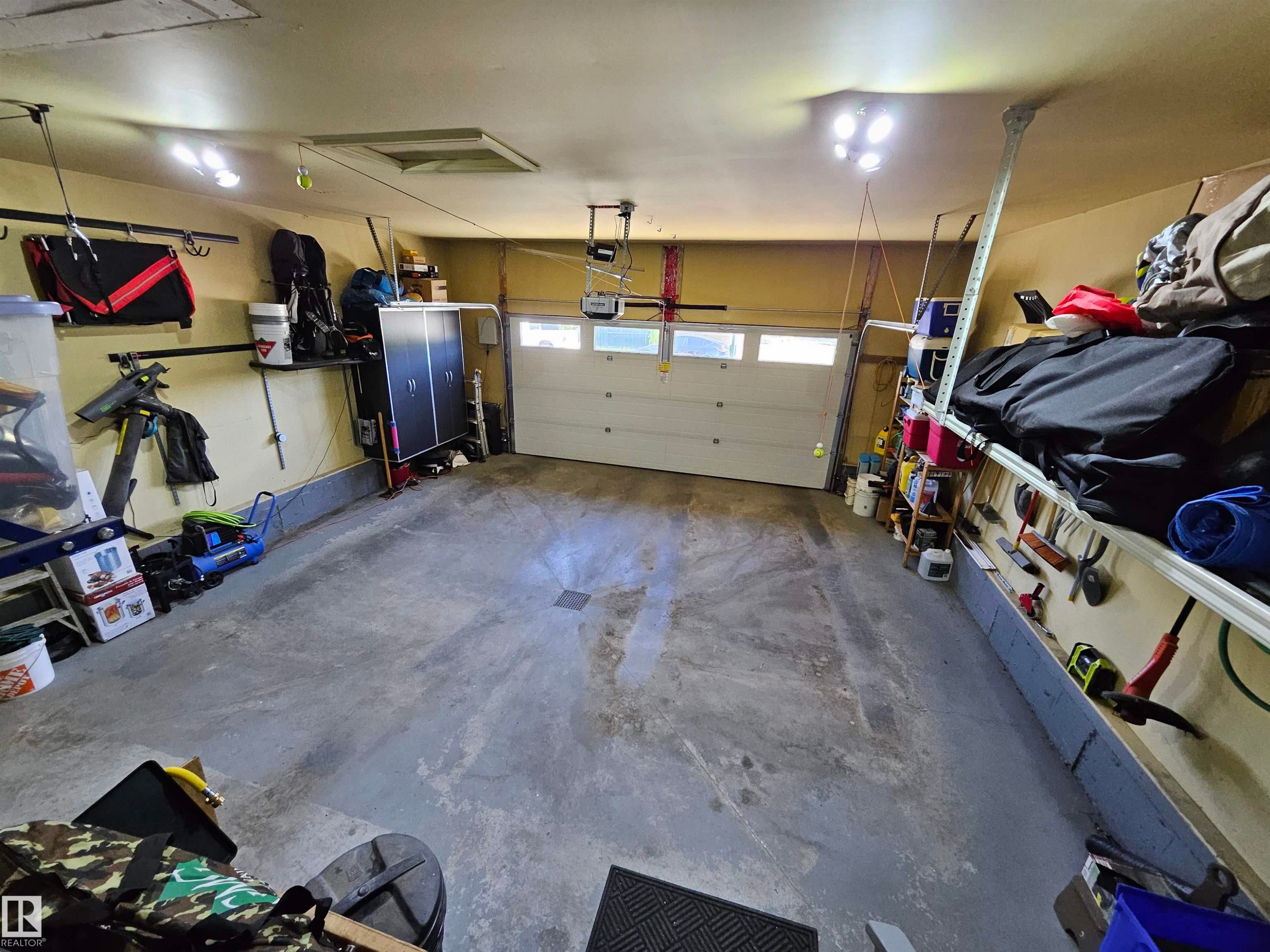 Spacious garage featuring a light-colored sectional overhead door with windows, a concrete floor, and integrated overhead lighting - 2322 Rutherford Way, Edmonton, AB
