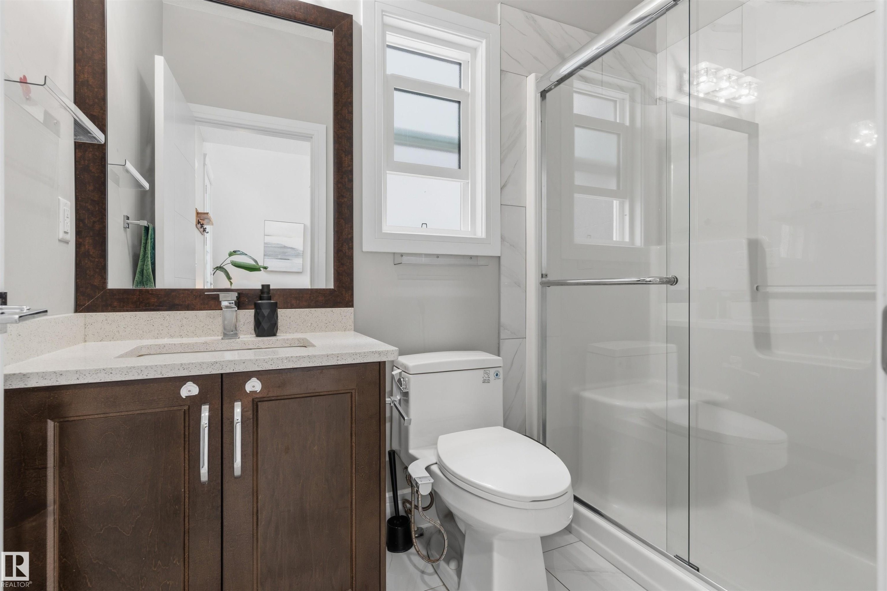 Bathroom featuring a glass-enclosed shower, a vanity with a light-toned countertop, and a framed mirror - 3312 11 Avenue, Edmonton, AB