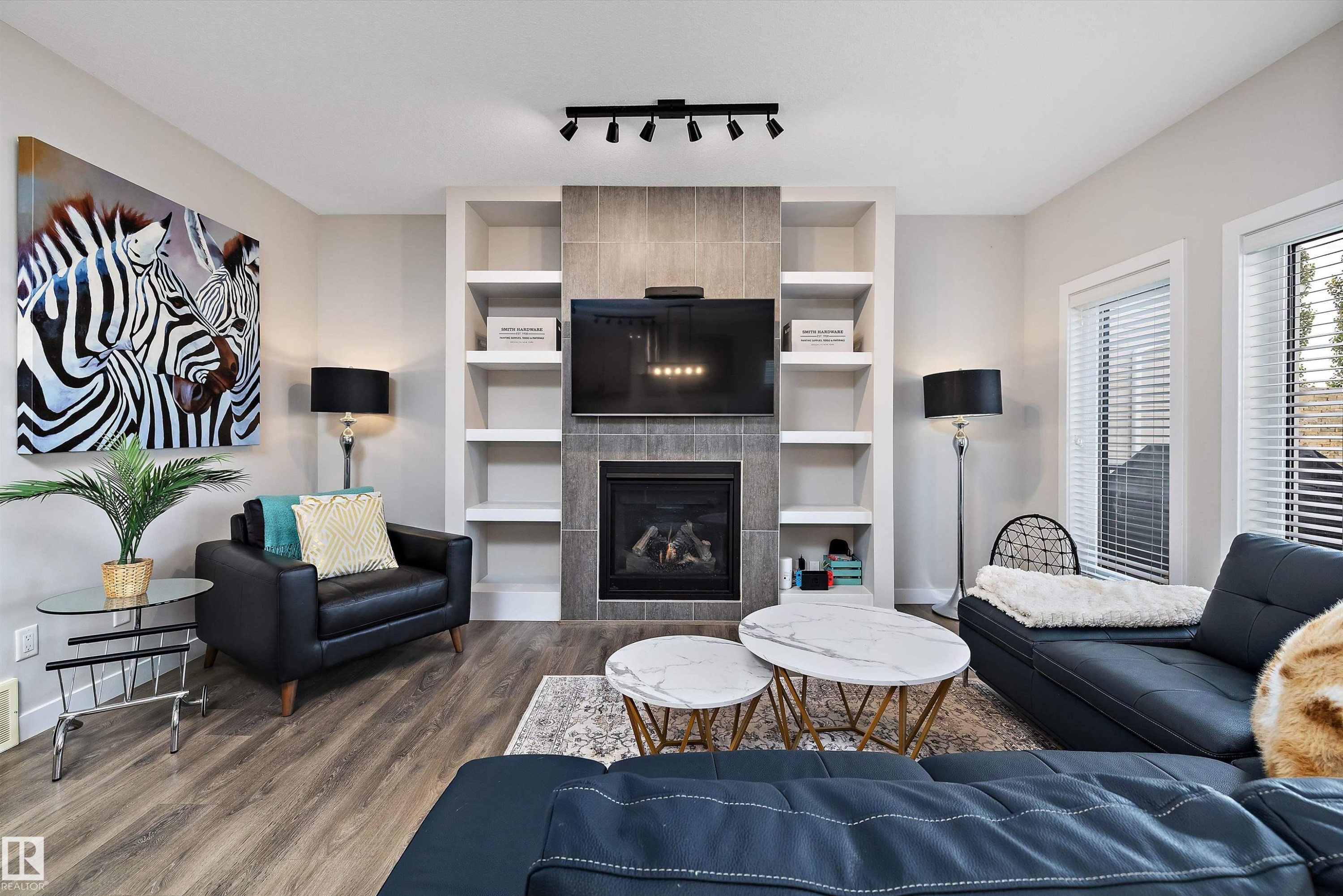 Living area featuring a fireplace with a tiled surround, integrated shelving, and track lighting - 363 Cy Becker Boulevard, Edmonton, AB - Indoor Photo Showing Living Room With Fireplace