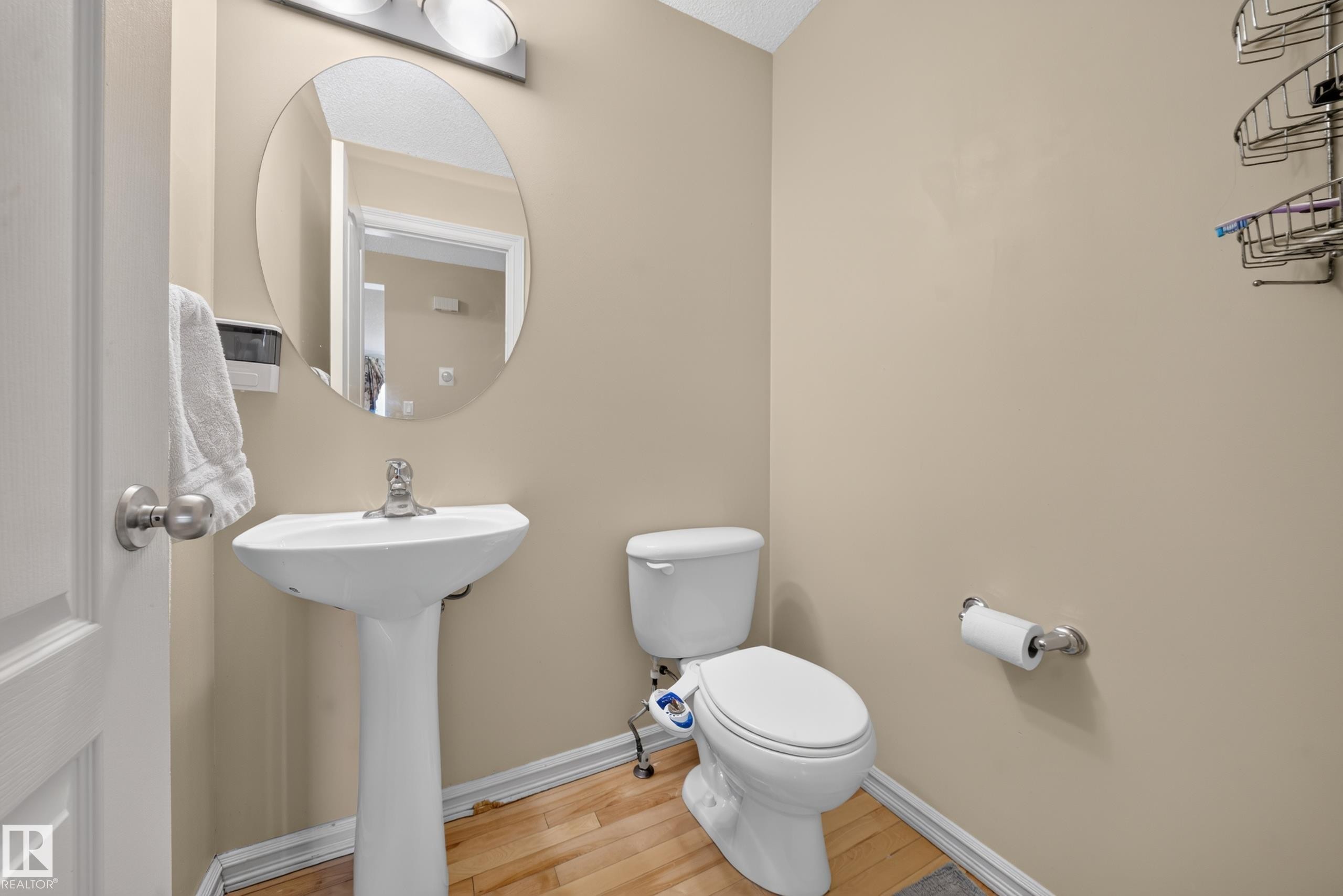 Powder room featuring a pedestal sink with a chrome faucet, oval mirror, and wood-finish flooring - 2518 33A Avenue, Edmonton, AB