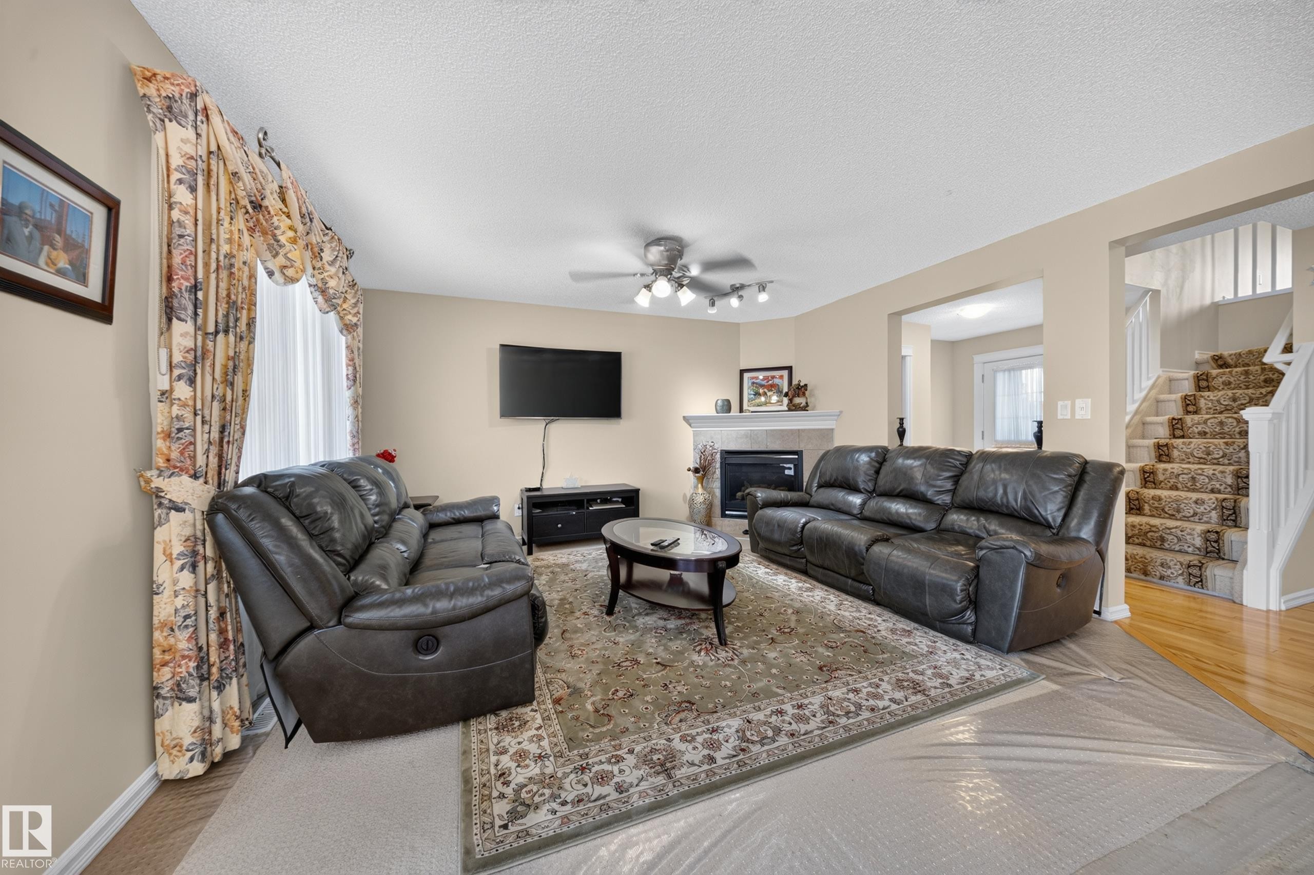 Living area featuring a corner fireplace with a white mantel, light-colored walls, and a ceiling fan with integrated lighting - 2518 33A Avenue, Edmonton, AB