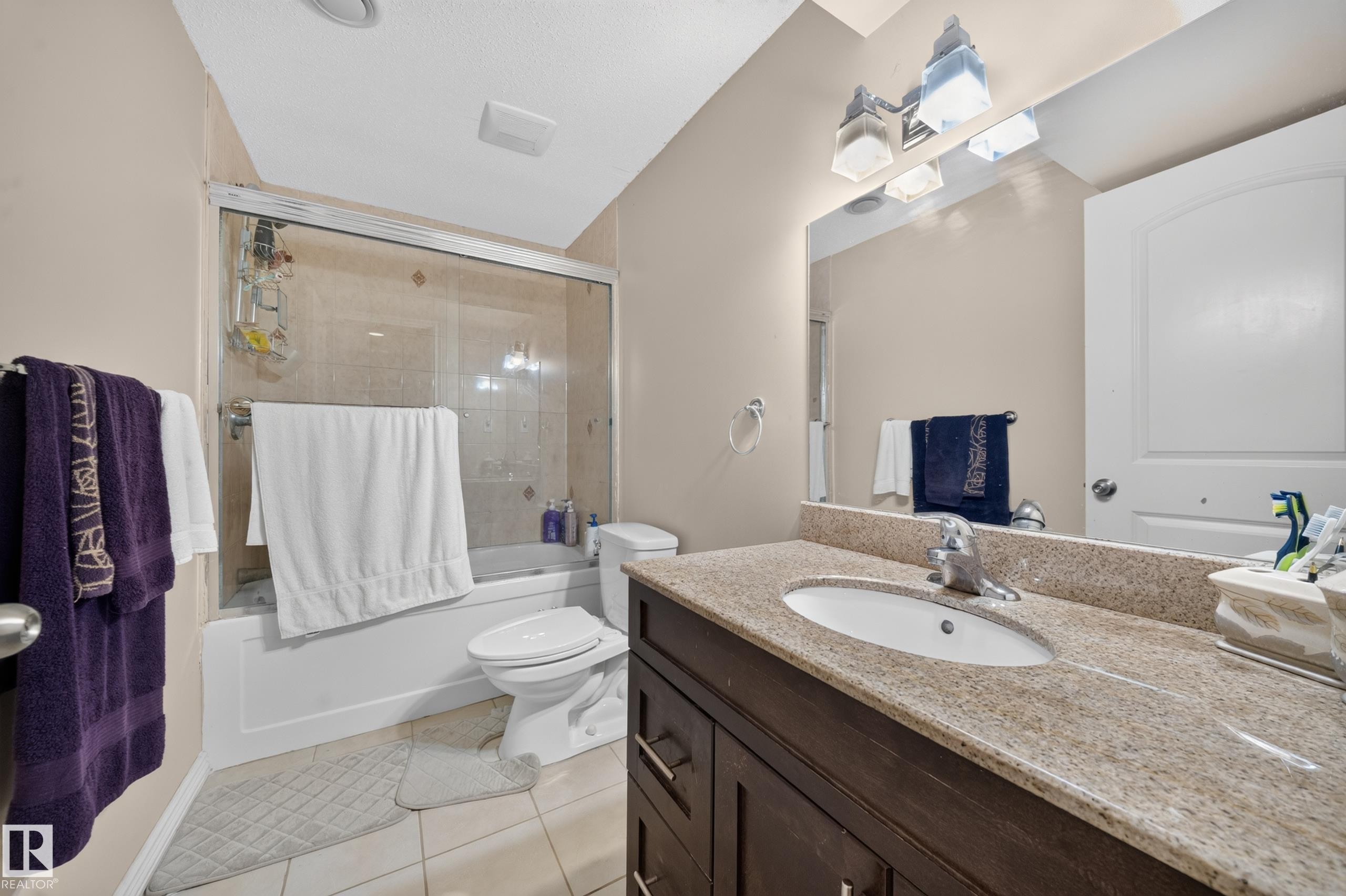 Bathroom featuring a granite-finish vanity with an undermount sink, a dark wood-finish cabinet, and a framed mirror with a contemporary light fixture - 2518 33A Avenue, Edmonton, AB