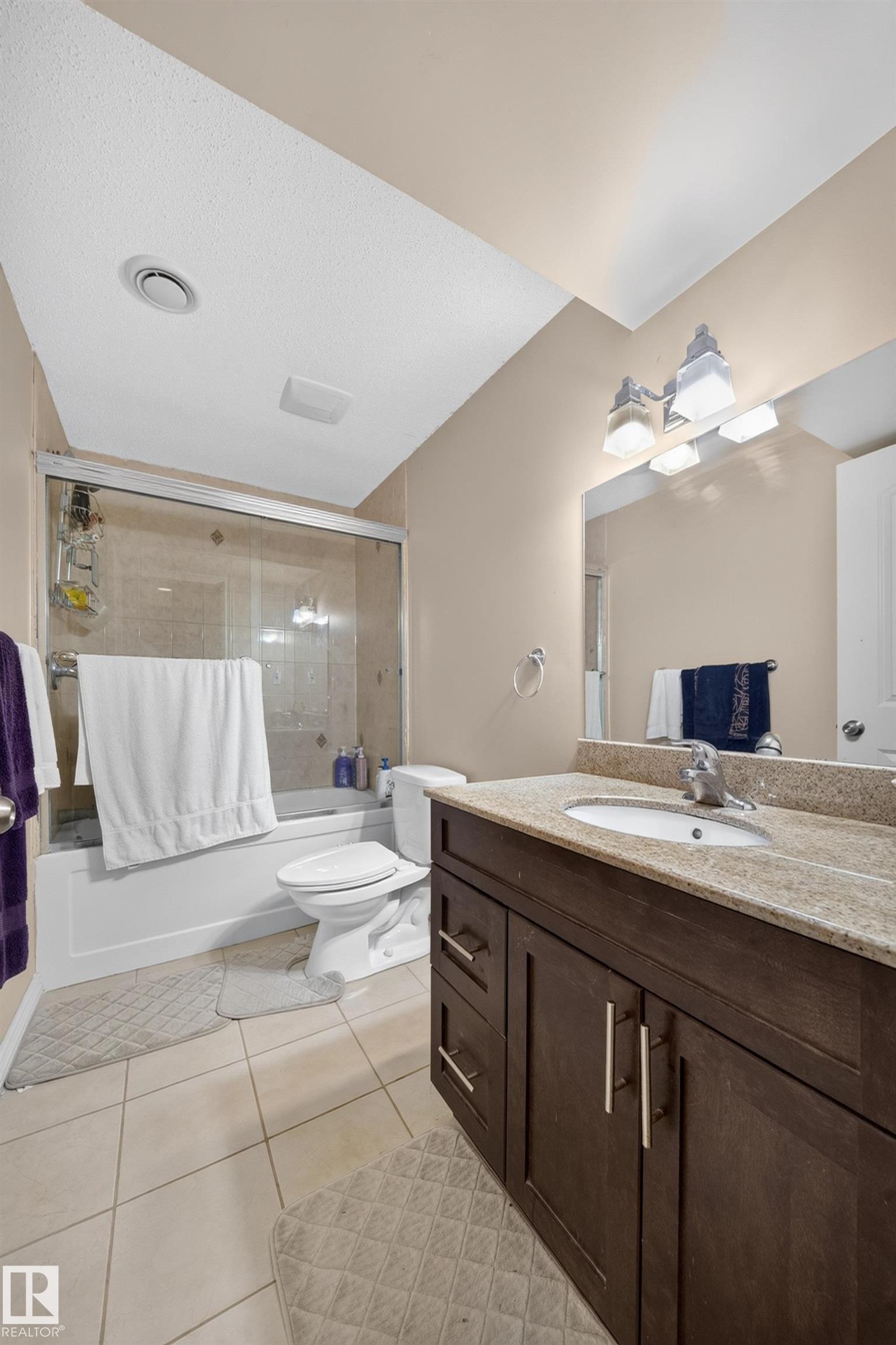Contemporary bathroom featuring a dark wood-finish vanity with a light-toned stone countertop, an integrated sink, and a chrome faucet - 2518 33A Avenue, Edmonton, AB