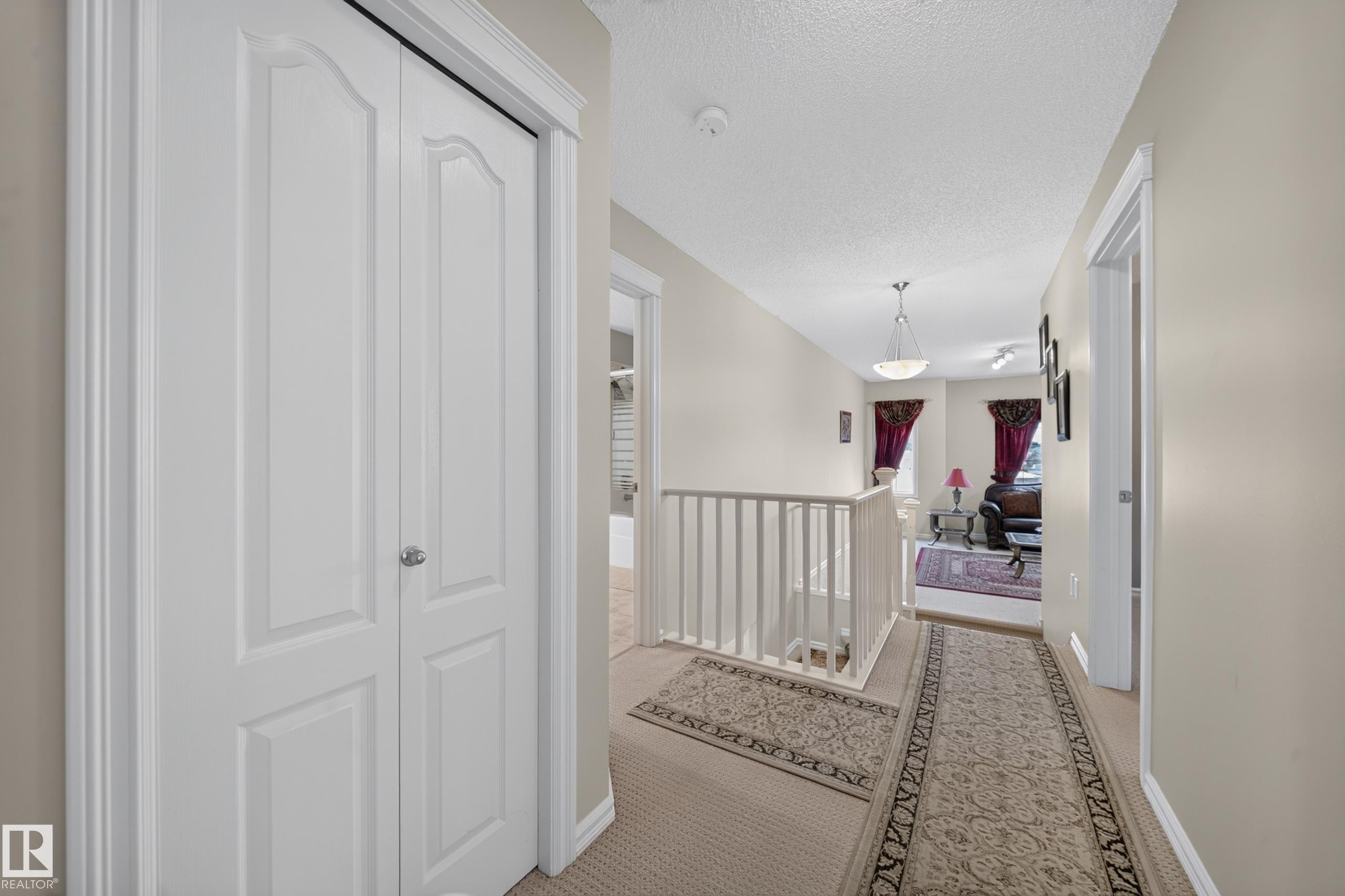 Hallway with neutral wall paint, carpet flooring, white bi-fold closet doors, and white railing - 2518 33A Avenue, Edmonton, AB