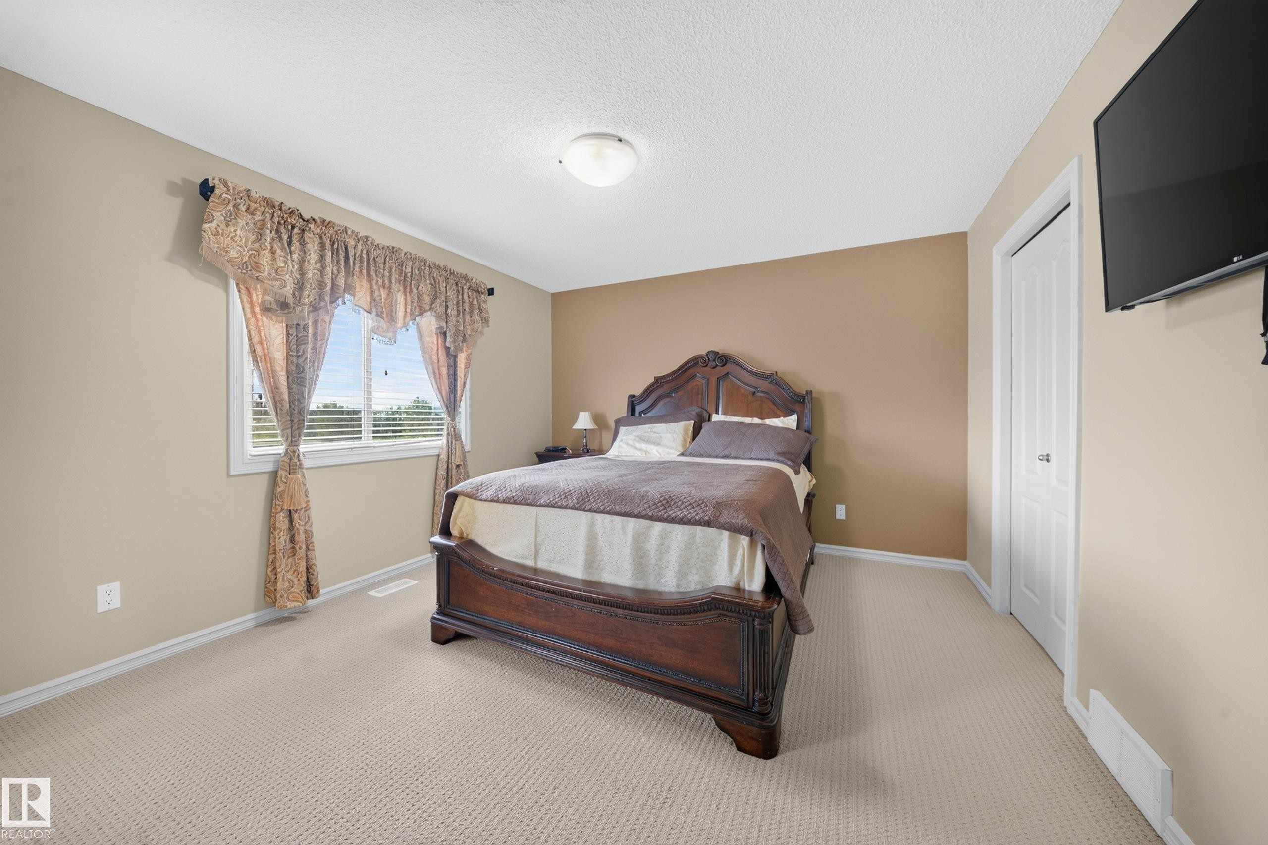 Carpeted bedroom featuring neutral wall tones, a white window frame with integrated blinds, a white bi-fold closet door, and a ceiling-mounted light fixture - 2518 33A Avenue, Edmonton, AB